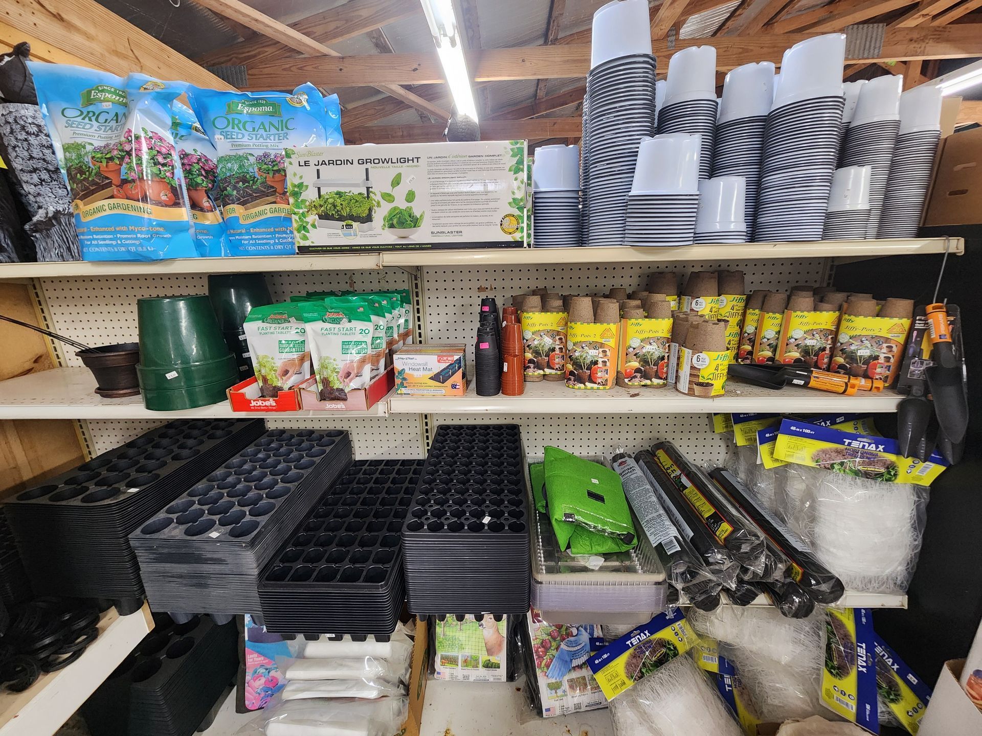 Shelved camping supplies and cookware in a store aisle, with stacked pots, trays, and packaged items