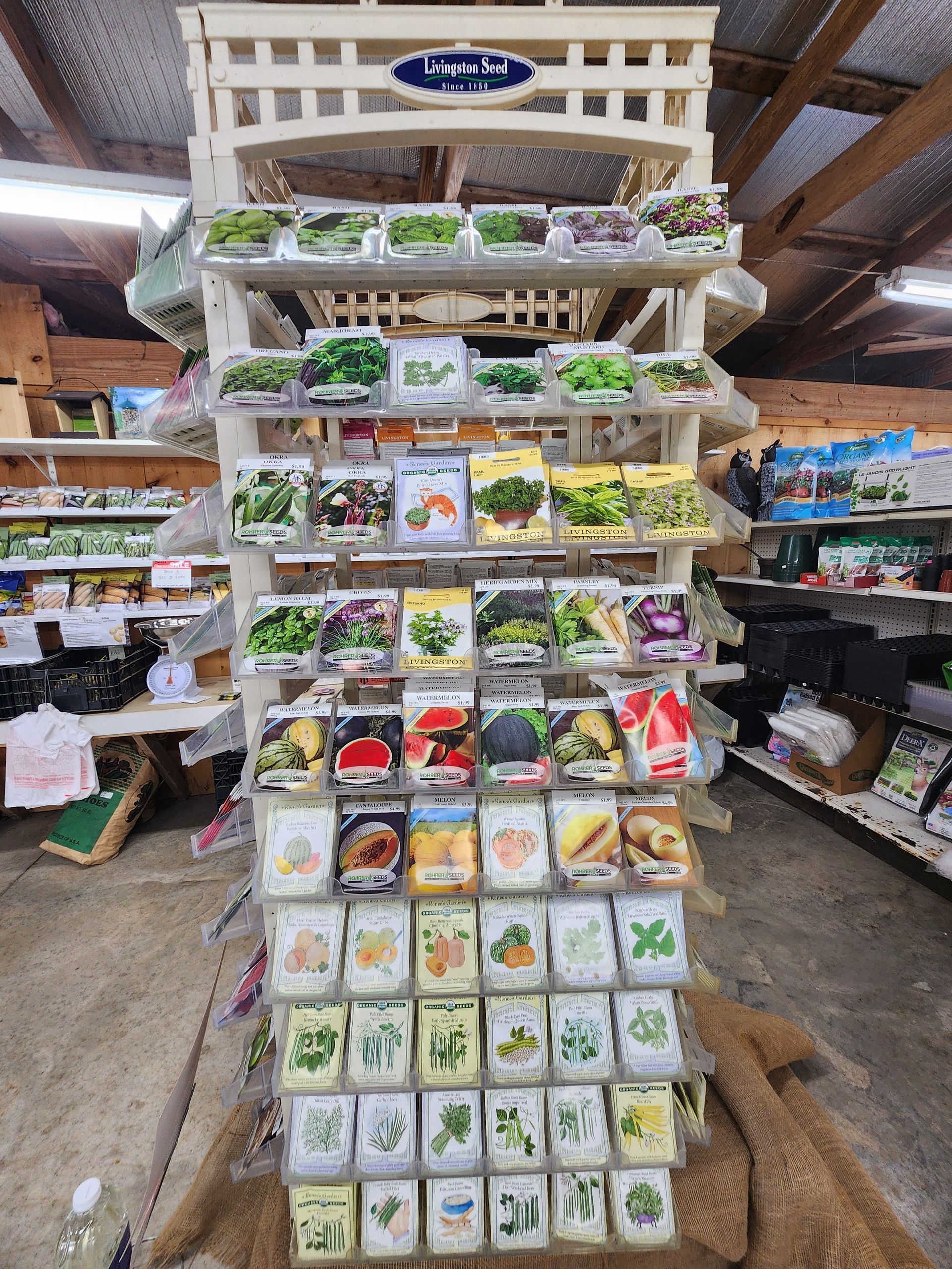 Garden center display of assorted potted plants and seedlings on a white rack in a greenhouse/market aisle