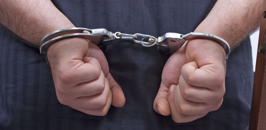 Handcuffed person’s clenched hands behind their back, framed by a courtroom bench