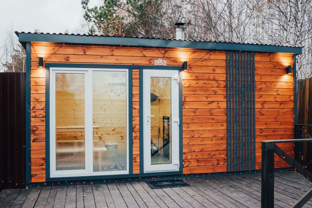Modern tiny house exterior with wood siding, large glass doors, and warm wall lights at dusk