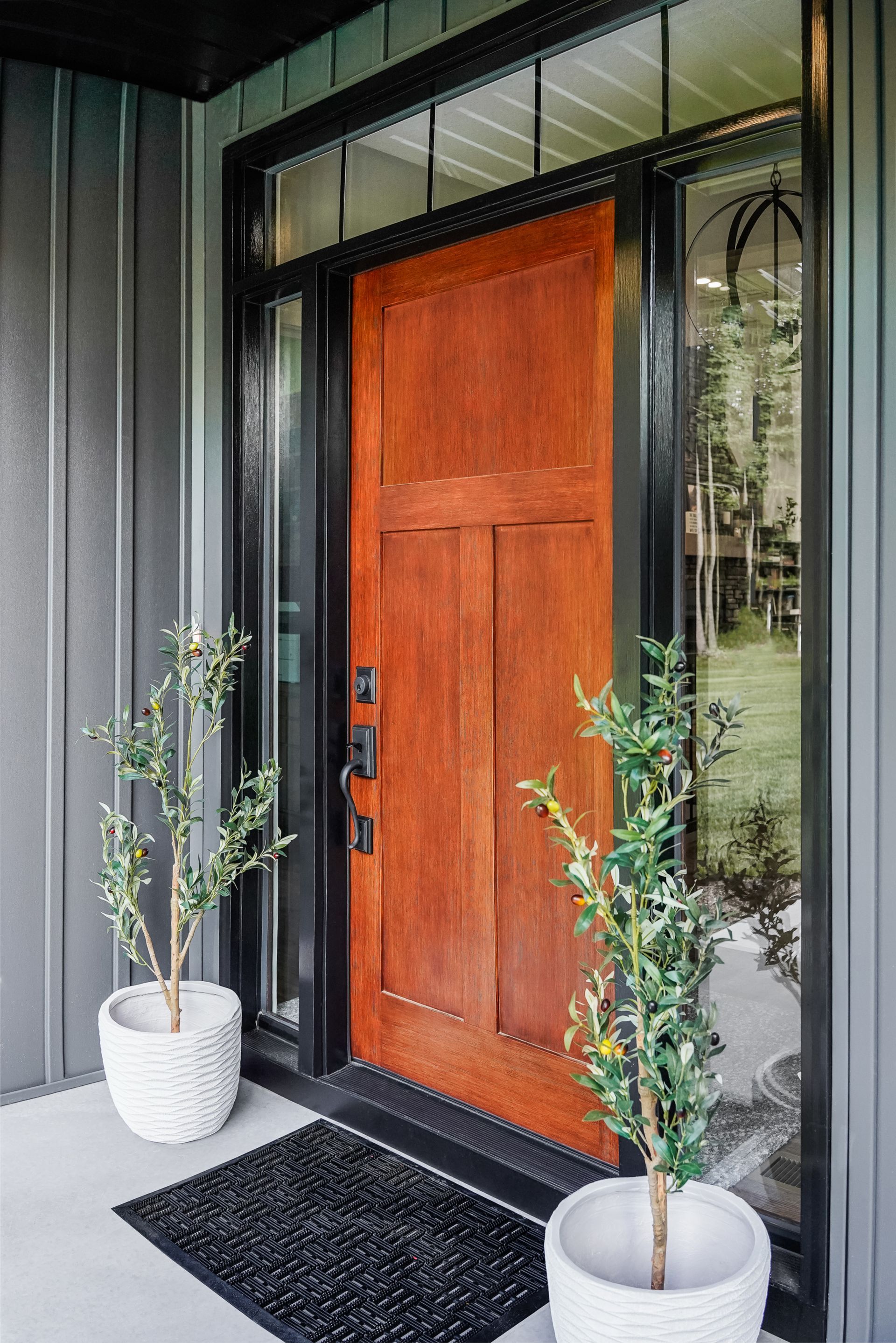 Front entry with a wooden door, black trim, potted plants, and a dark doormat