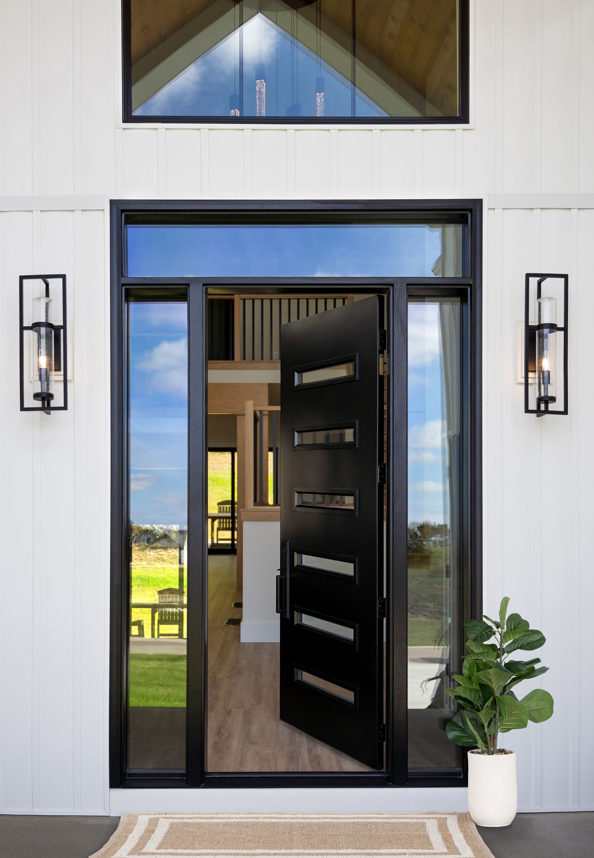 Open black front door with sidelights, showing a bright interior and a potted plant by the entry