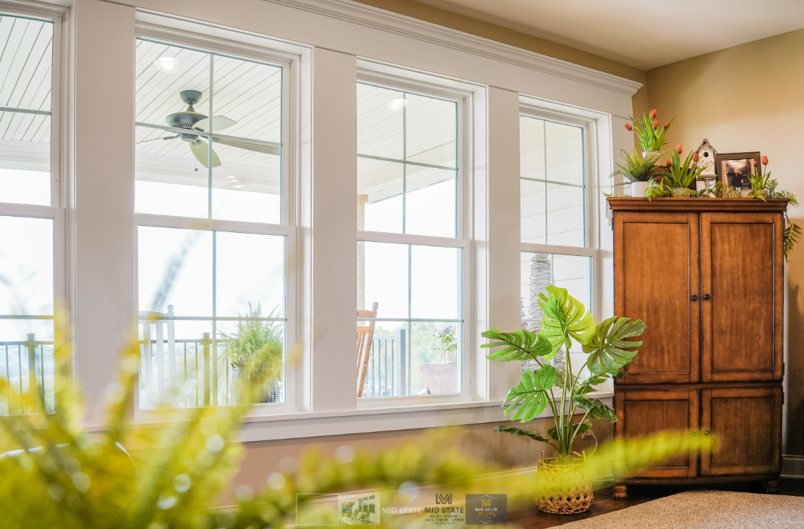 Bright living room with large windows, a ceiling fan, and a wooden cabinet near potted plants.