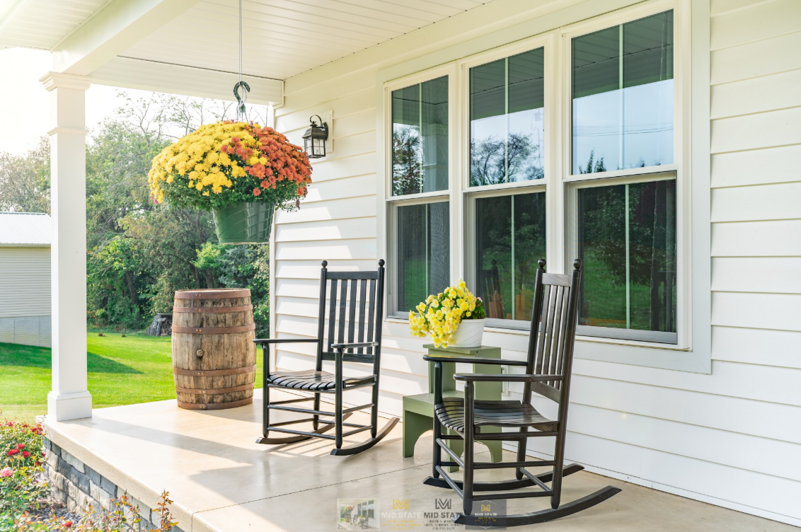 Porch with two black rocking chairs, potted flowers, and large windows on a white house