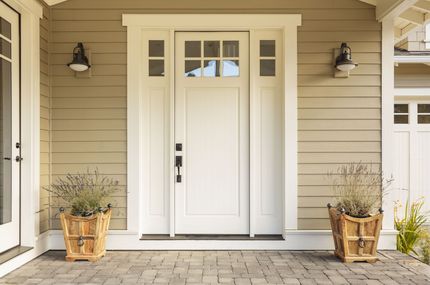 Front porch with white double doors, wall lanterns, and potted plants on a brick walkway