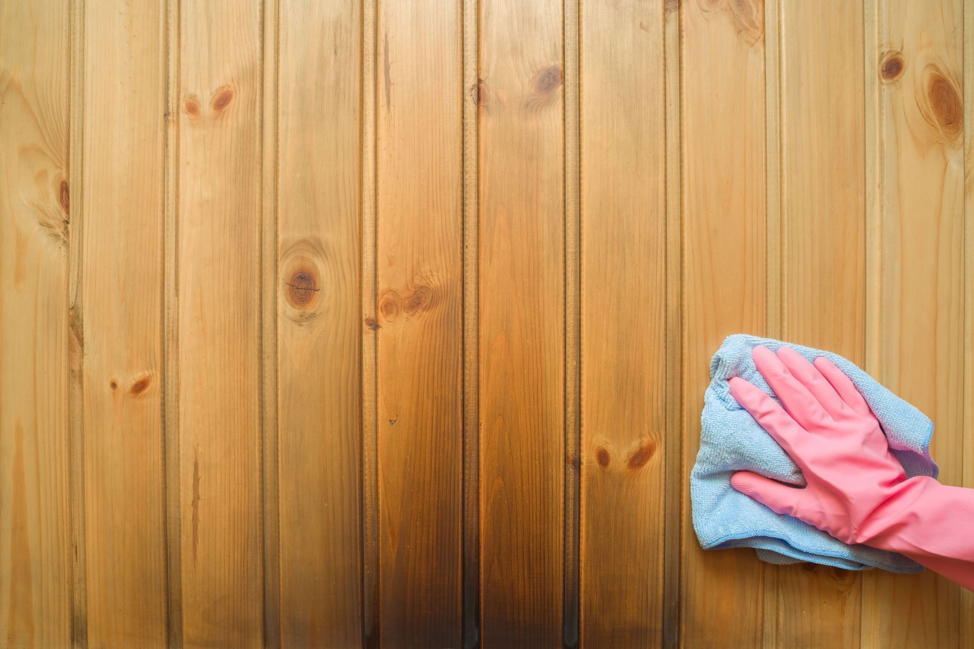 A person wearing pink gloves is cleaning a wooden surface with a cloth.