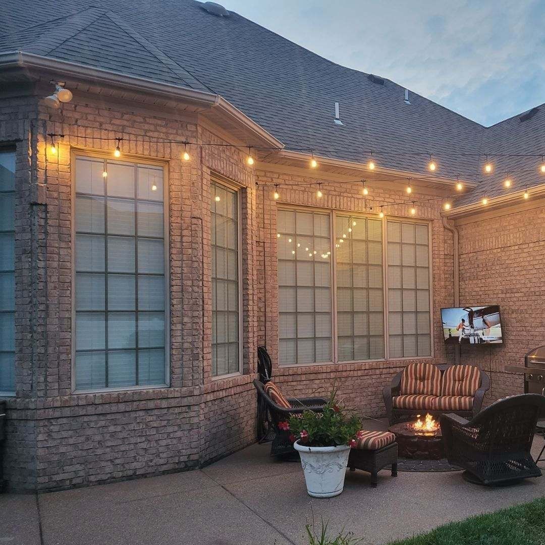 Brick patio with string lights, seating, potted plant, and a TV mounted on the wall.
