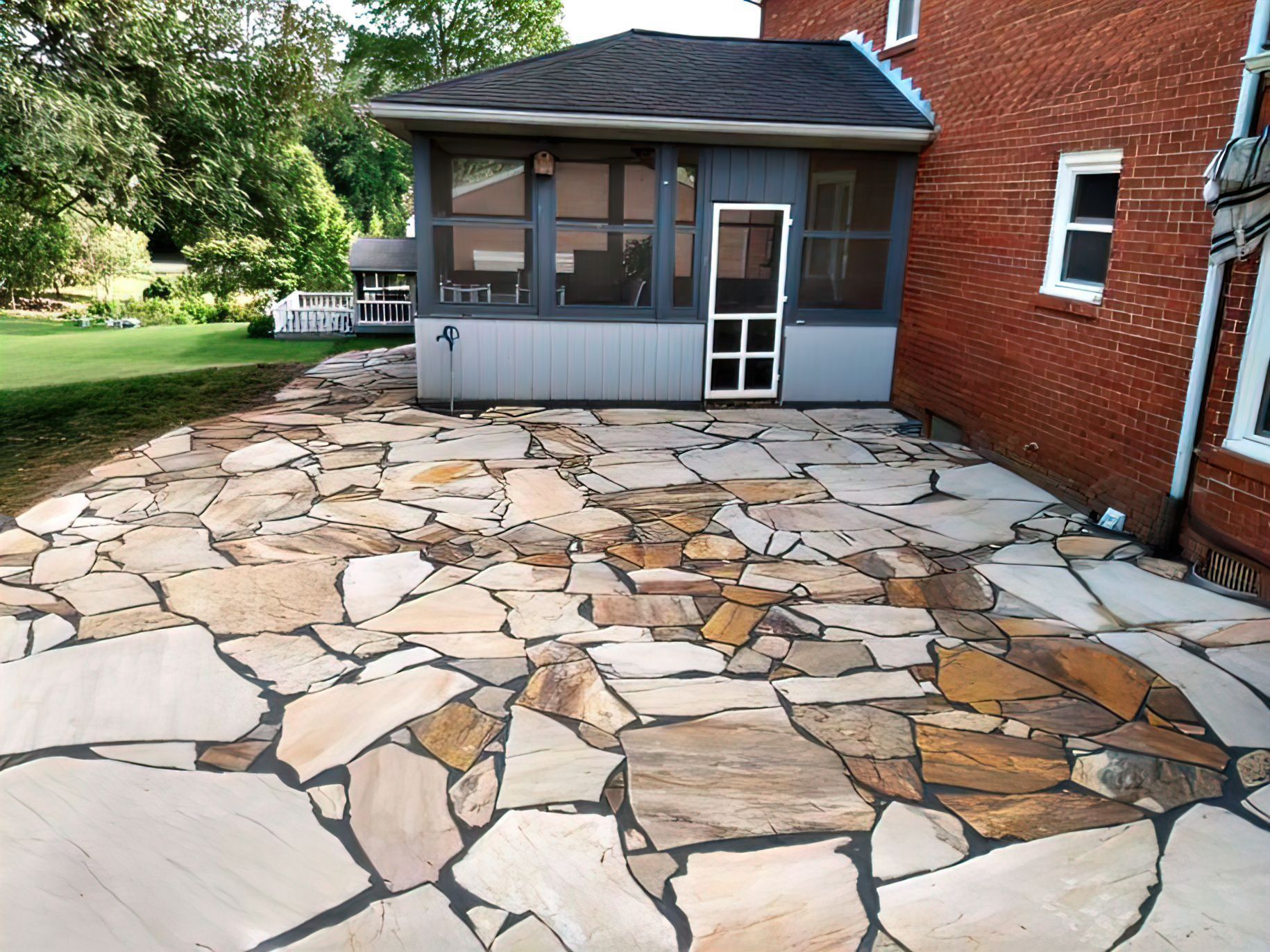 Flagstone patio next to a brick house with a screened porch.