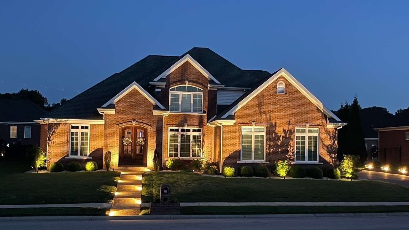 Brick house at dusk with outdoor lighting highlighting the facade and landscaping.
