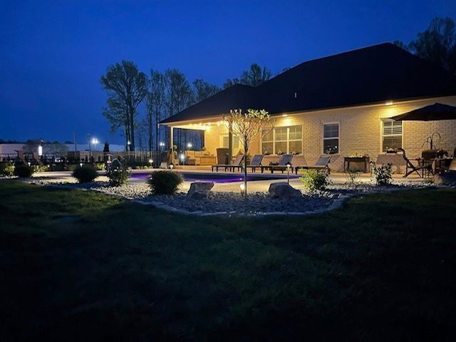 Nighttime backyard scene with illuminated pool, house, and landscaping.