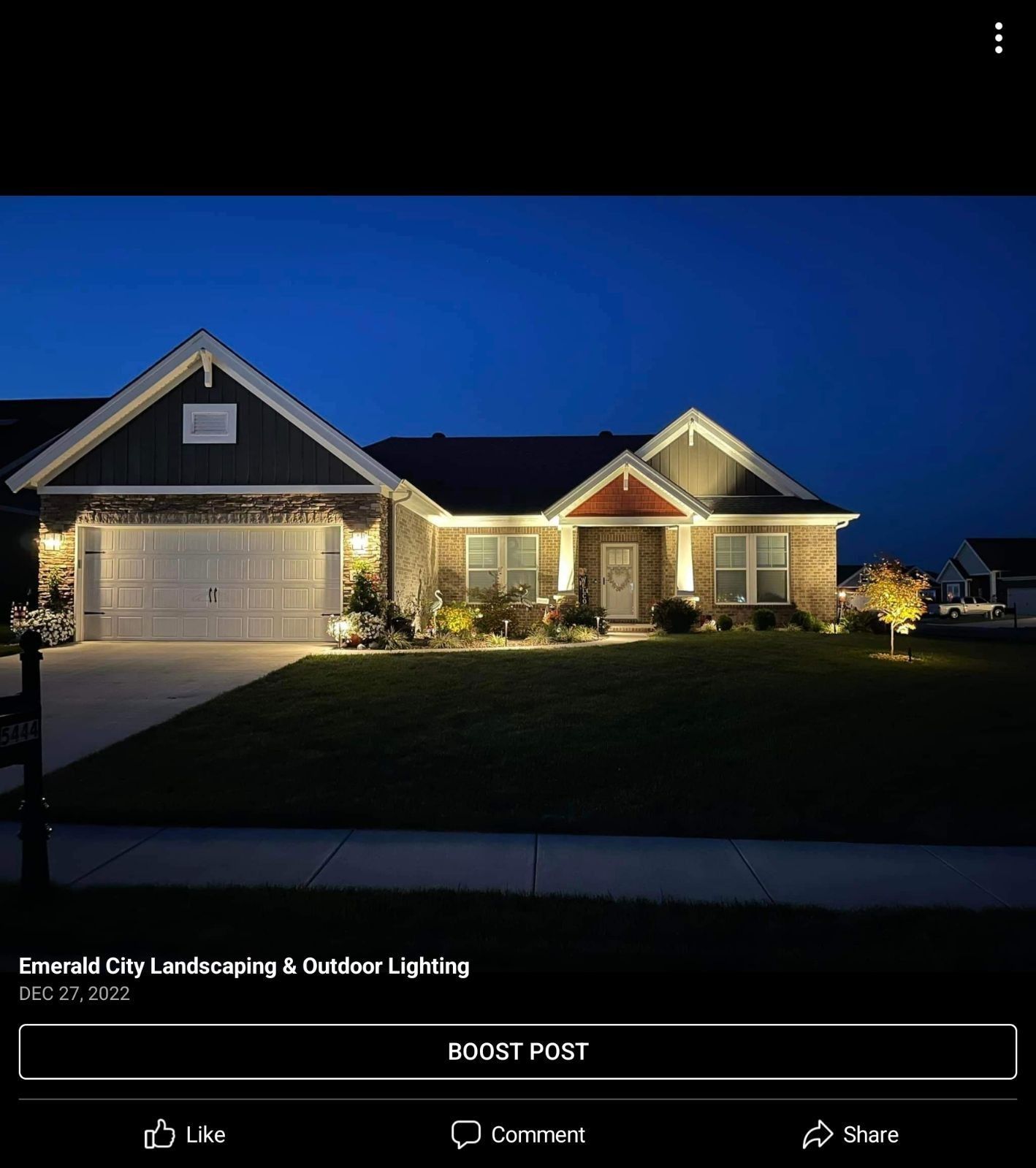 House with outdoor lighting at dusk. Front of home, dark blue sky. Green lawn.