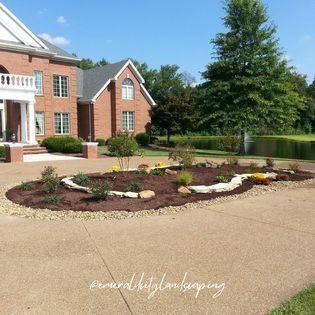 A landscaped garden bed in front of a large brick home with a curved driveway.