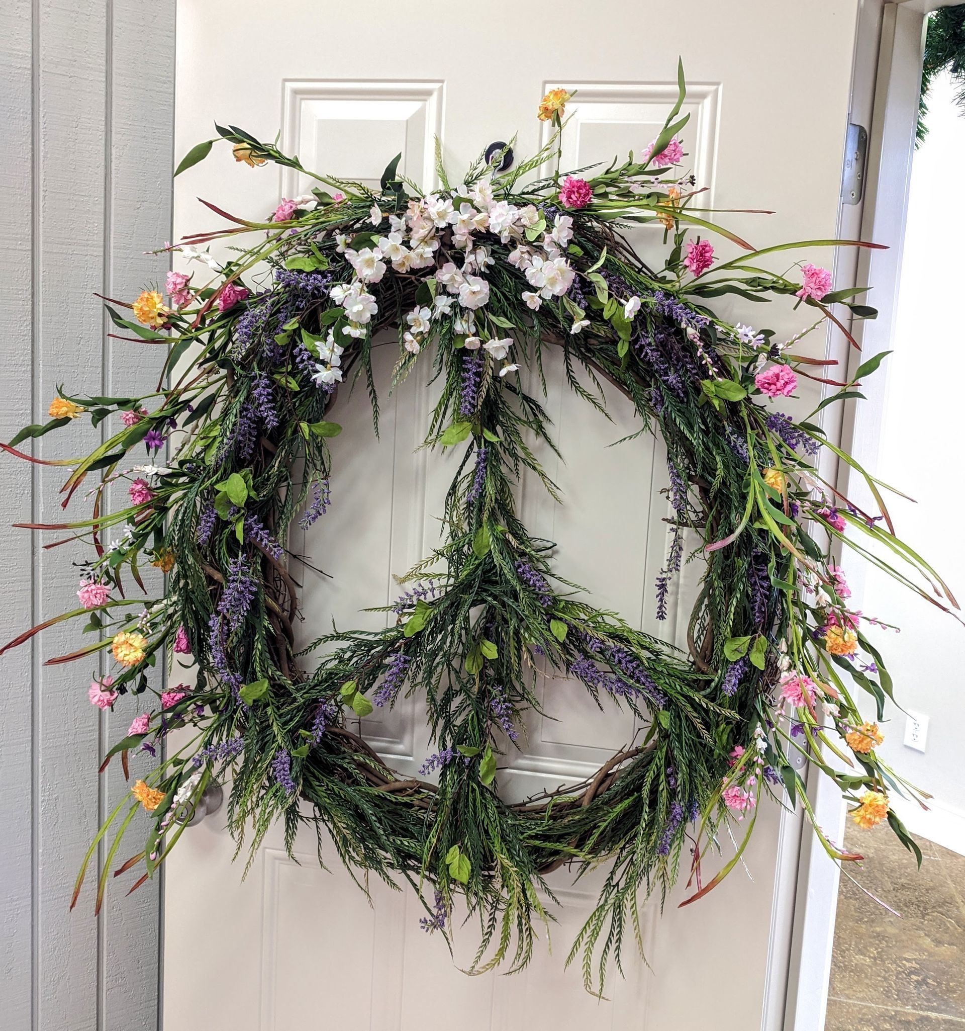 Peace sign wreath on a white door, made of flowers and greenery, with touches of pink and yellow.