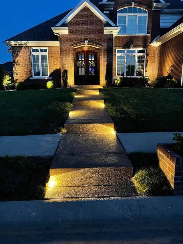 Lit walkway leading to a brick house with illuminated front door at night.