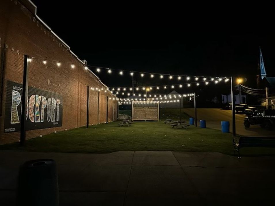 Outdoor patio at night with string lights, tables, and mural on a brick building.