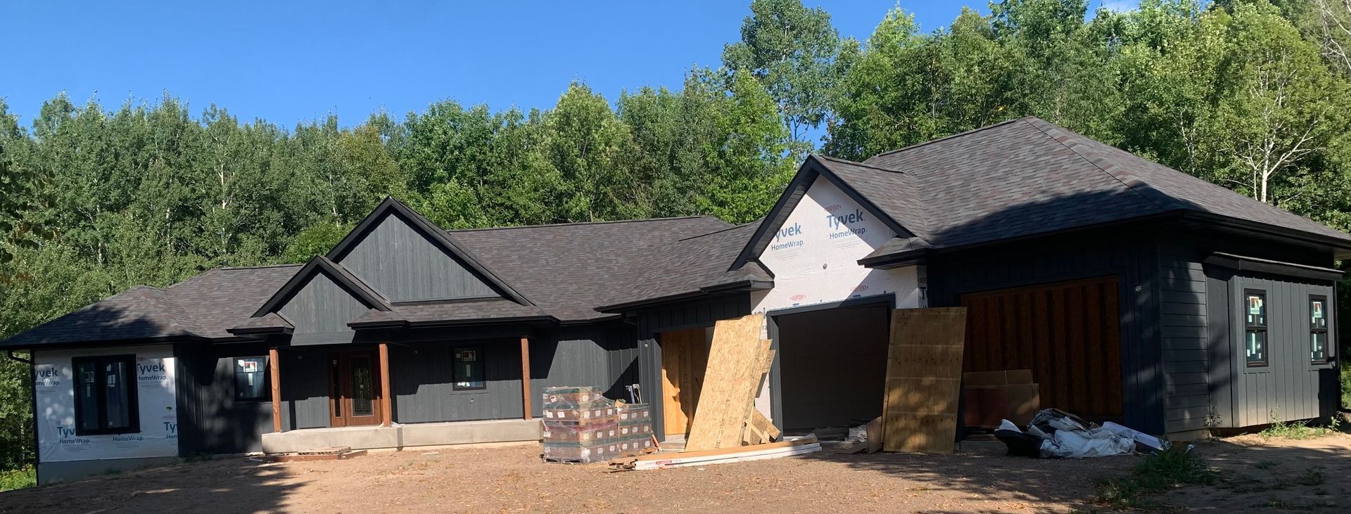 Single-story modern house with dark roof, light walls, and a wooden front porch under a blue sky.
