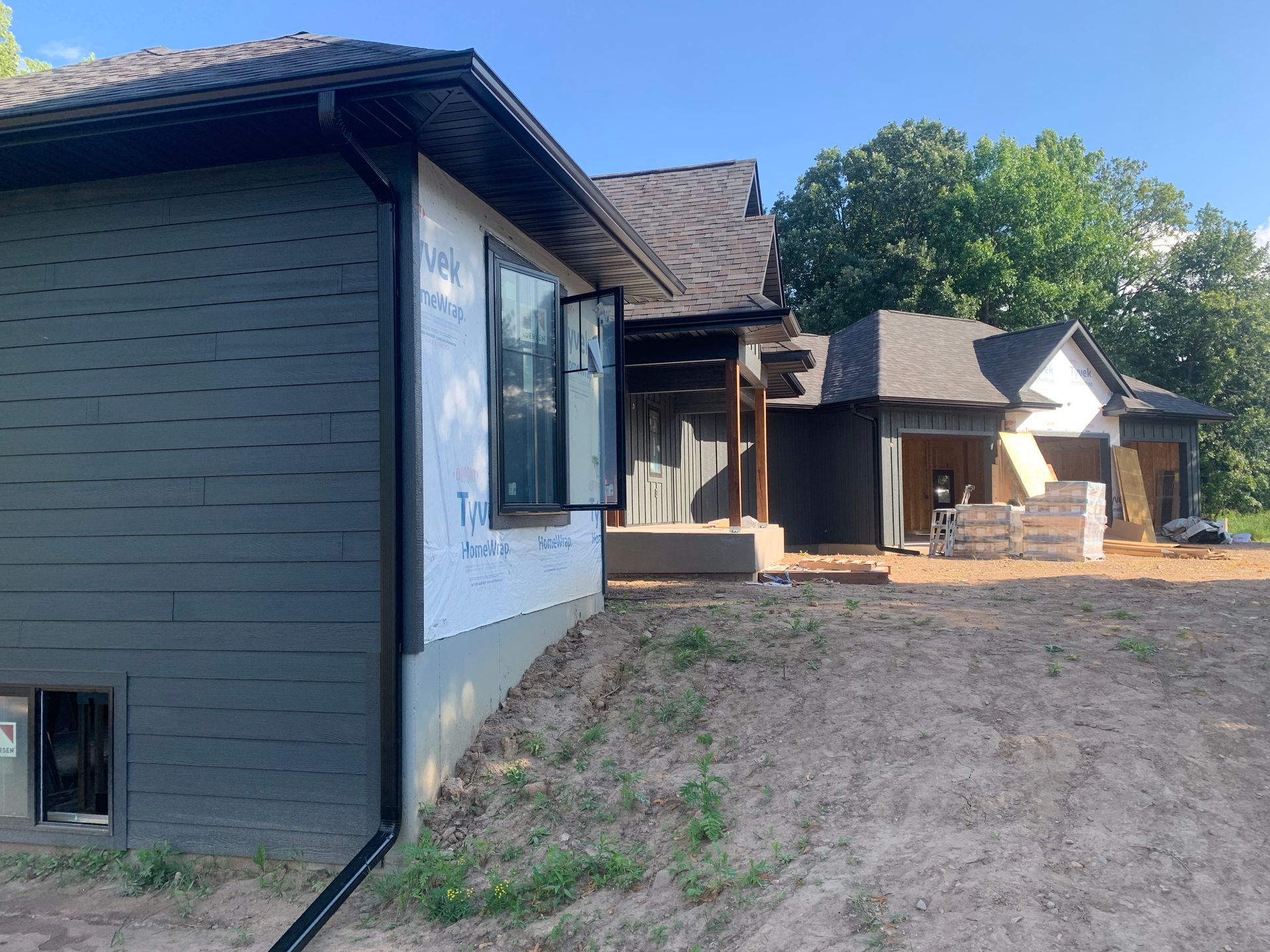 Exterior of a house with gray siding, brown roof, and a dirt yard under a clear sky