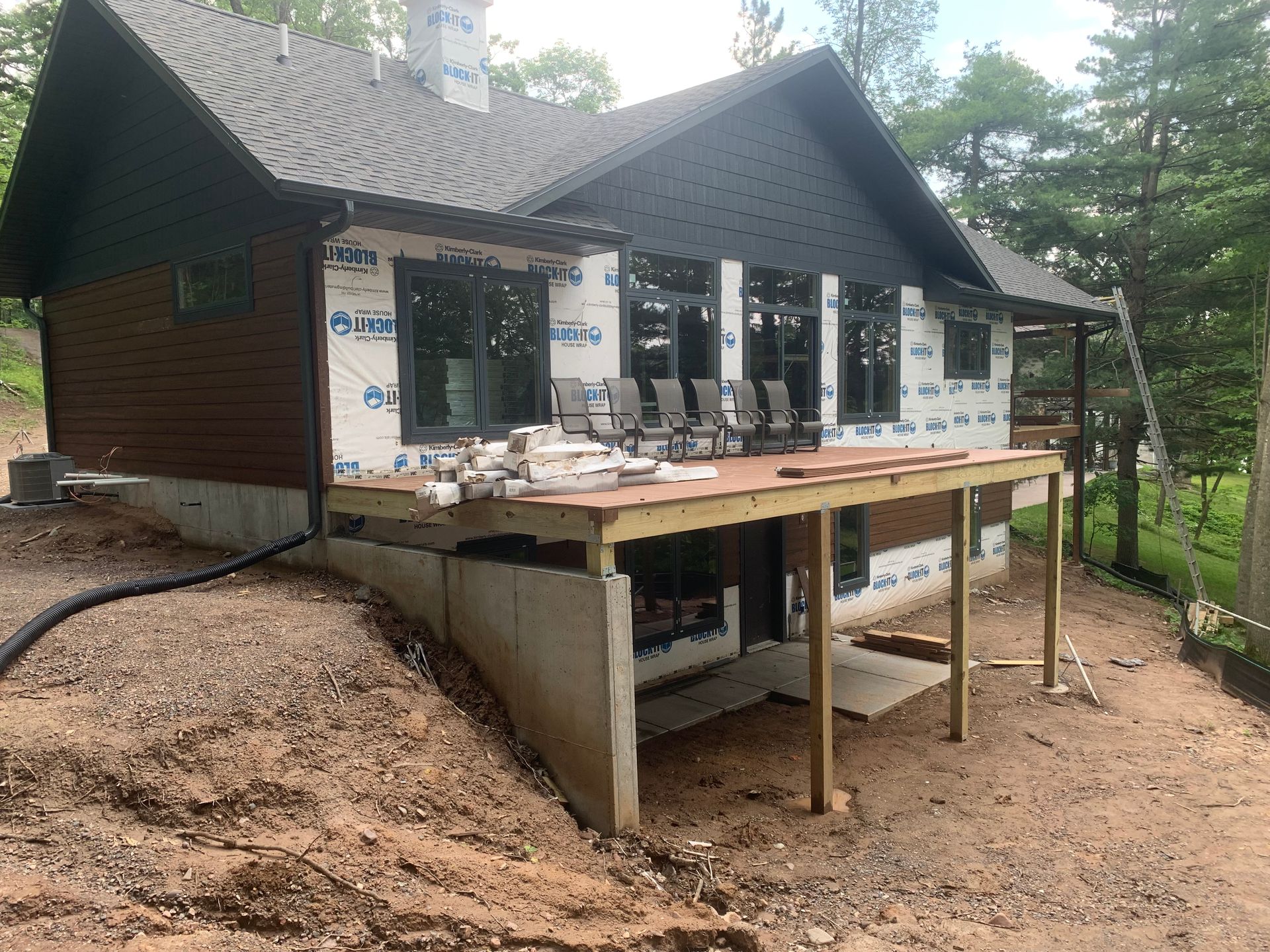 Small house under construction with unfinished wooden deck and concrete foundation on a dirt lot.