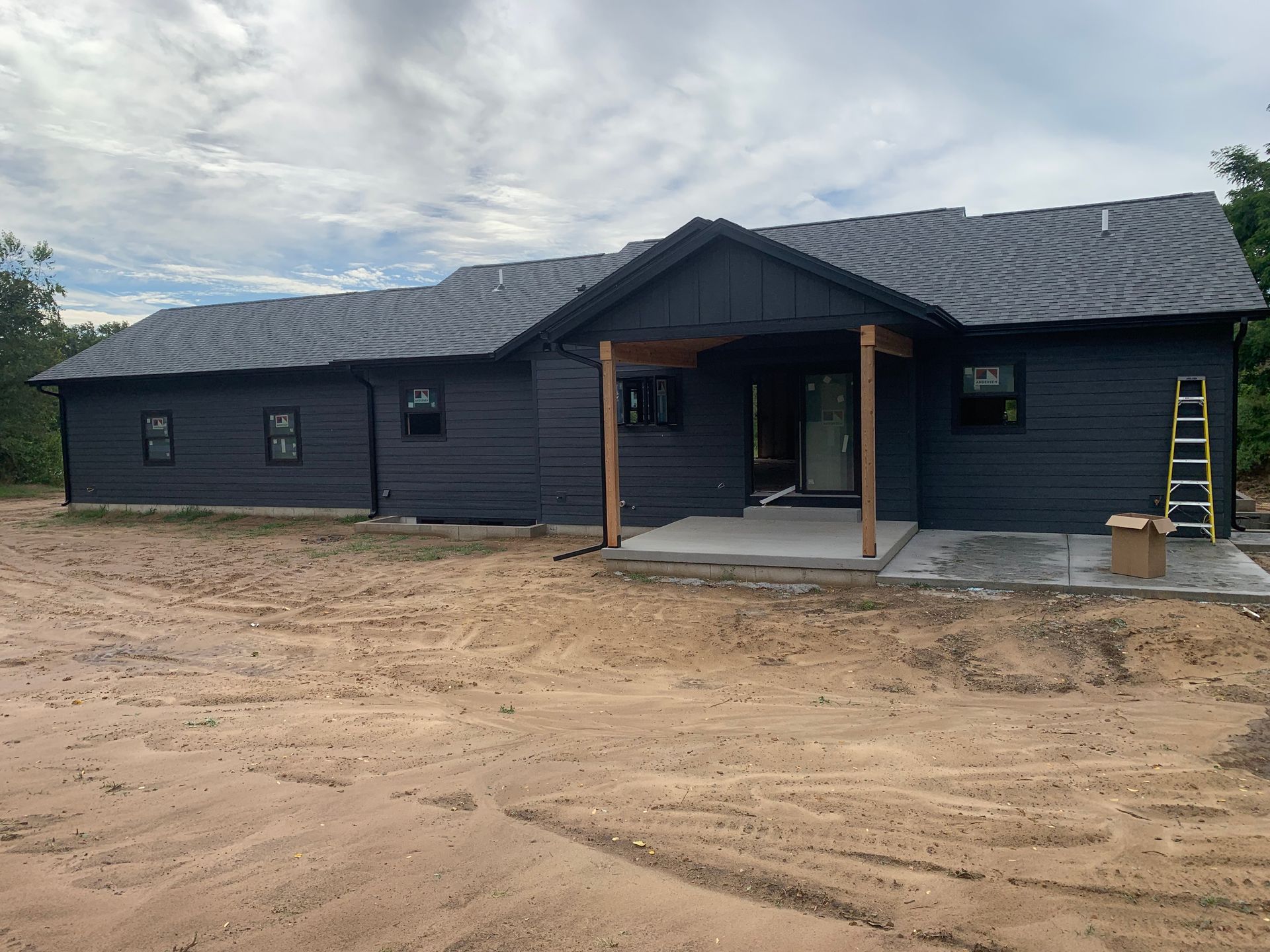 Dark blue single-story house under construction on a dirt lot, with a covered entry and ladder on the right