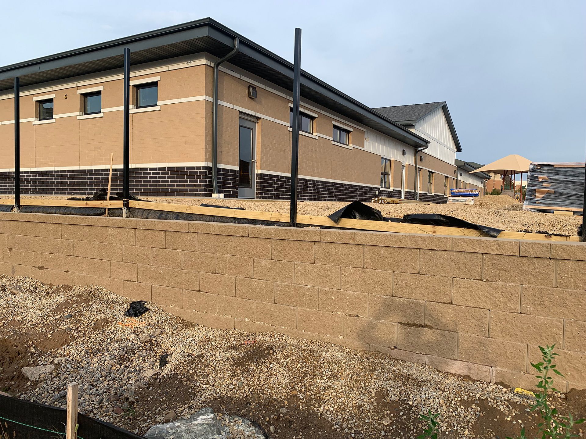 Single-story tan building under construction with black trim, dirt foreground, and a clear sky.