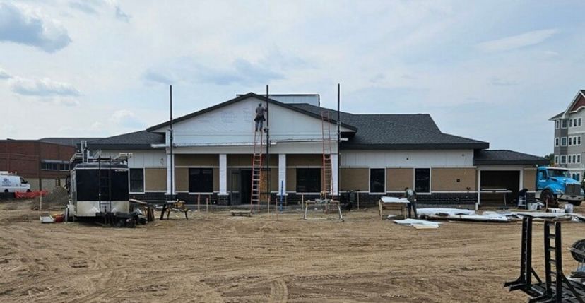 Single-story building under construction on a sandy lot, with scaffolding and materials in front.