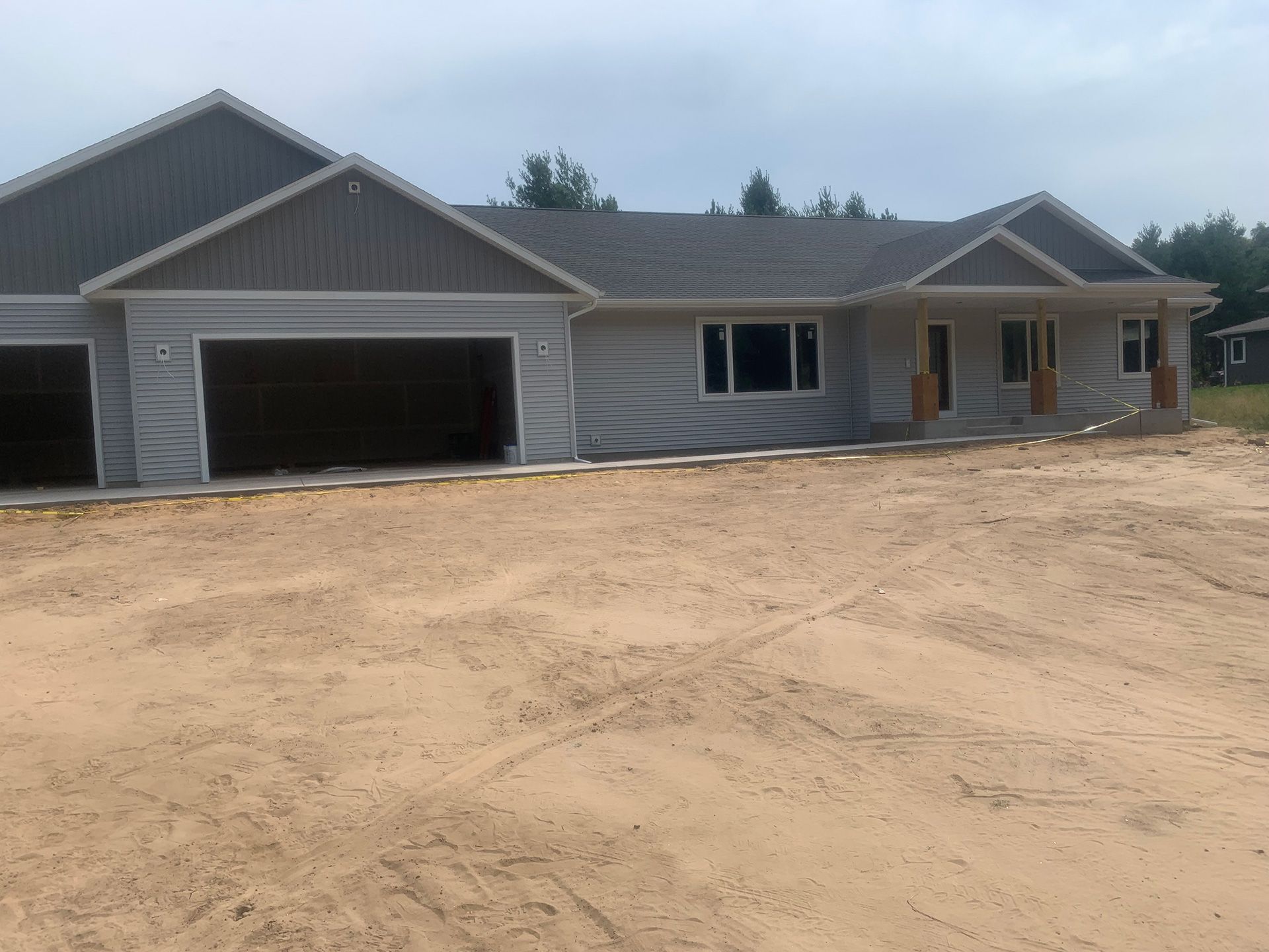 New gray single-story house with two-car garage on a dirt lot under construction