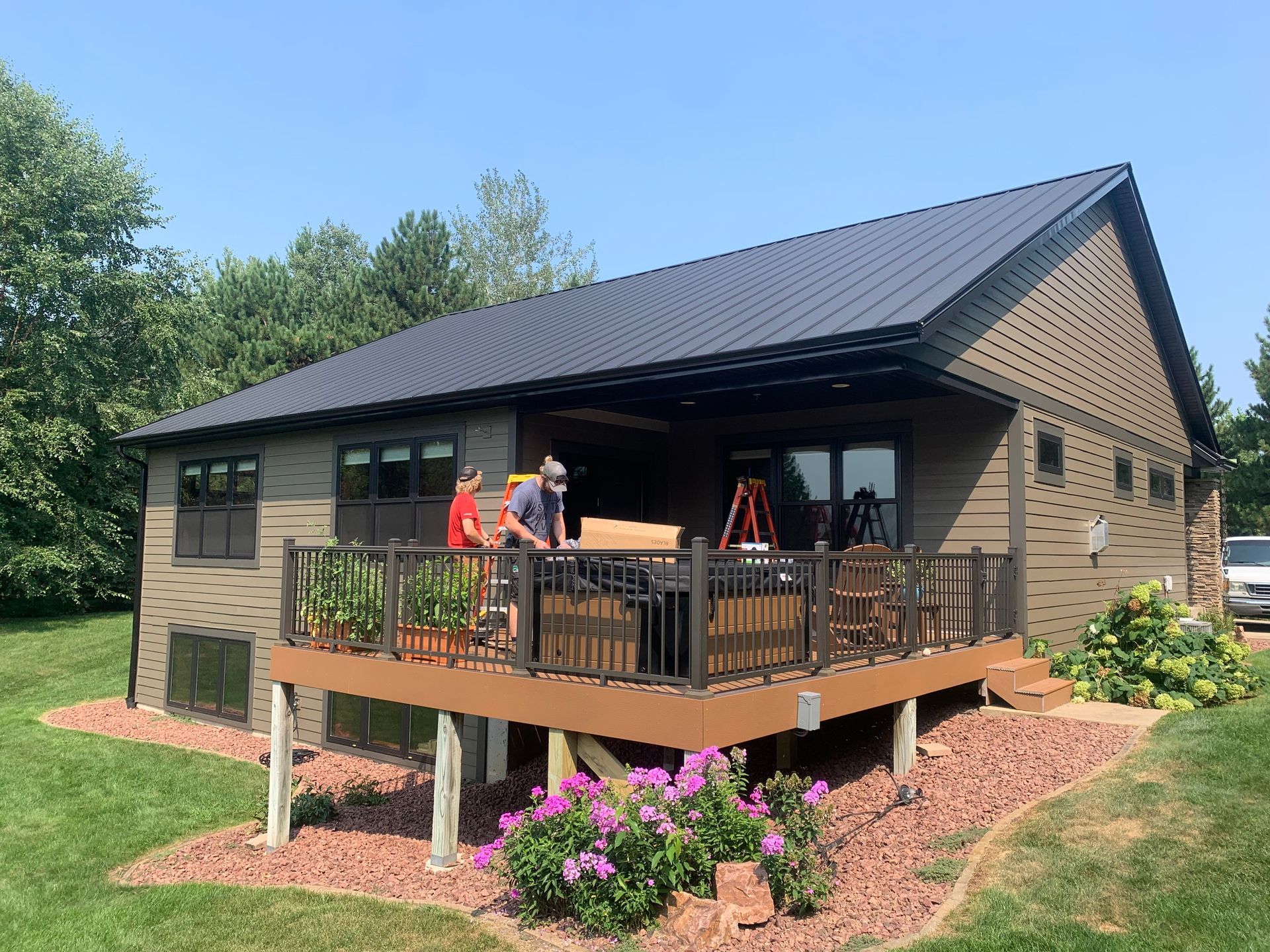 Modern house with a raised deck and two workers on the porch under a clear blue sky