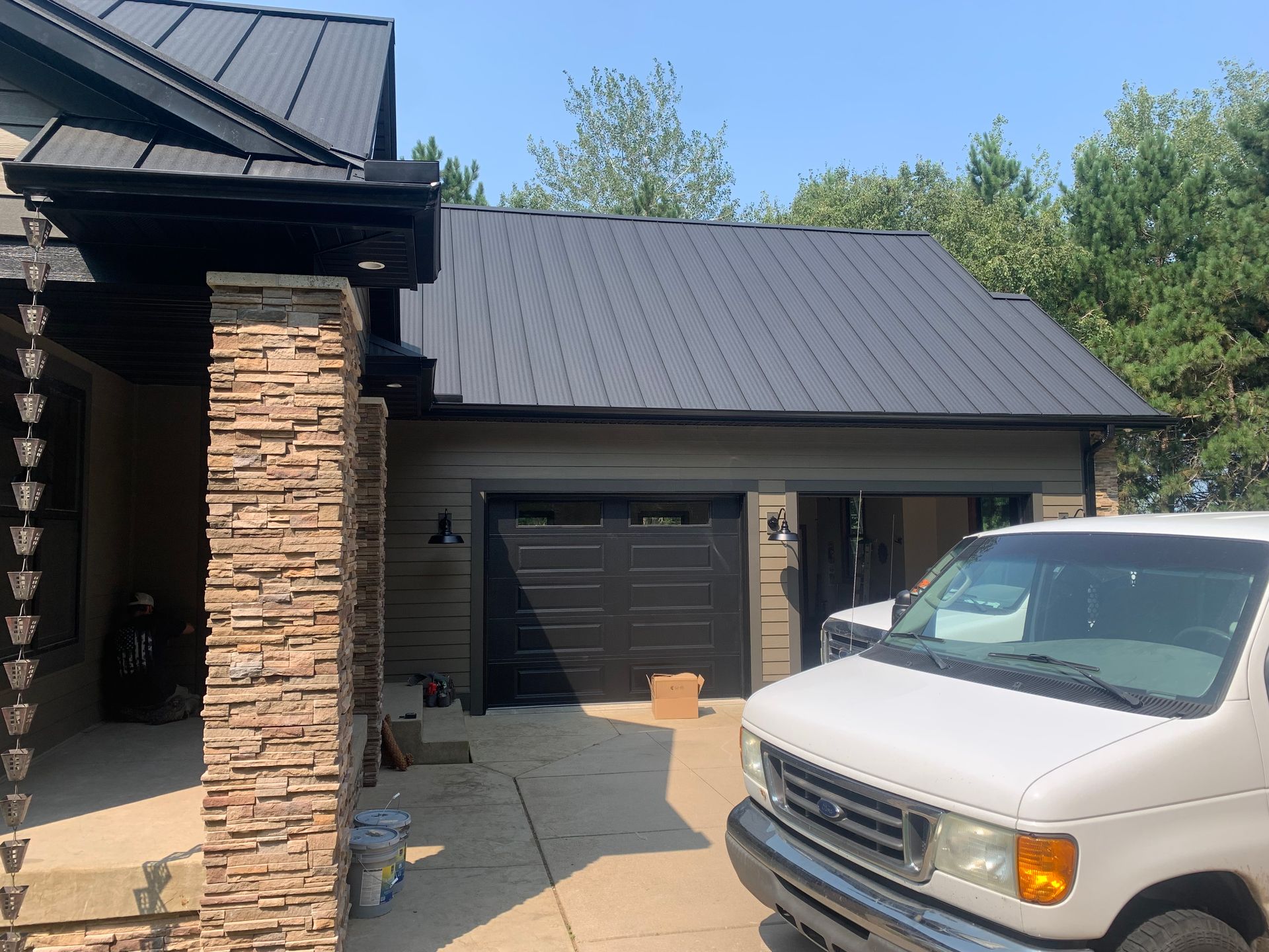 House exterior with stone column, dark metal roof, open garage, and white truck parked in driveway