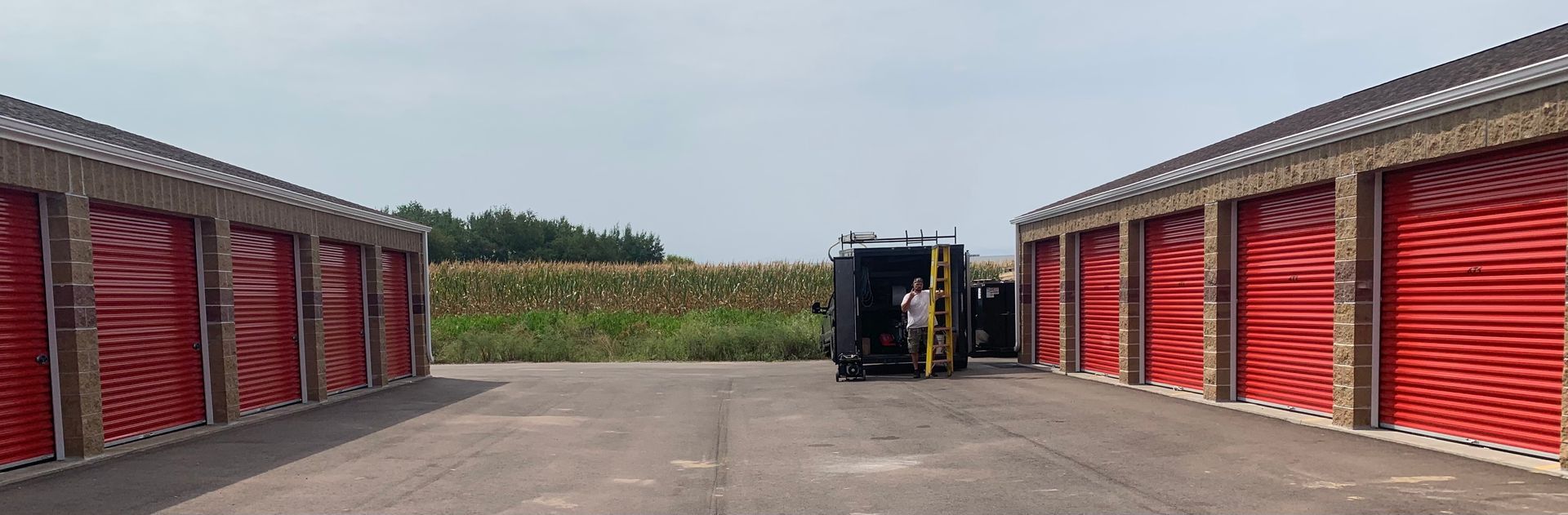 Open storage yard with red shipping containers on both sides and a forklift at the far end.