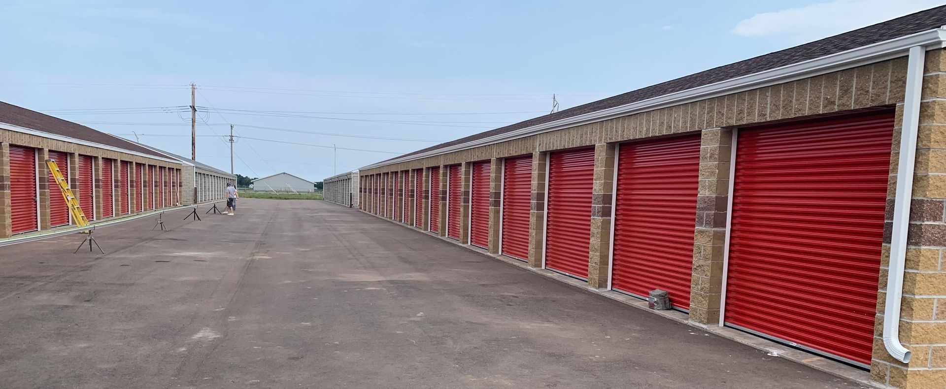 Row of red storage unit doors along a wide paved drive under a cloudy sky