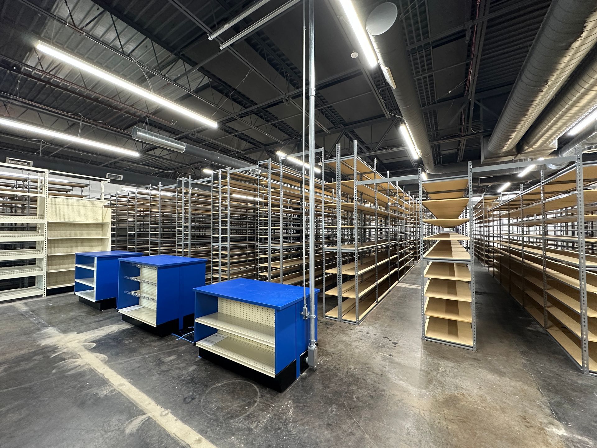 Empty warehouse aisle with metal shelving, blue carts, and overhead lights