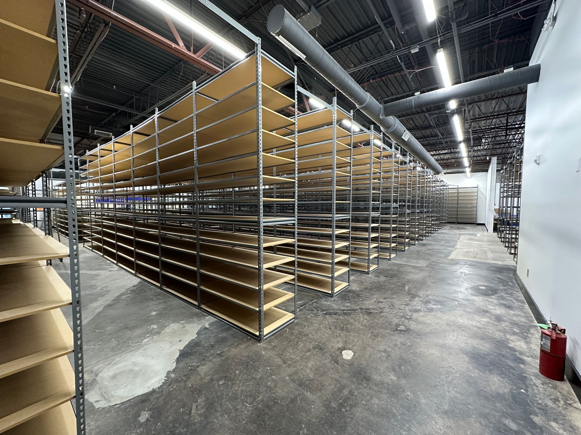 Rows of empty metal shelving in a warehouse aisle under bright industrial lights