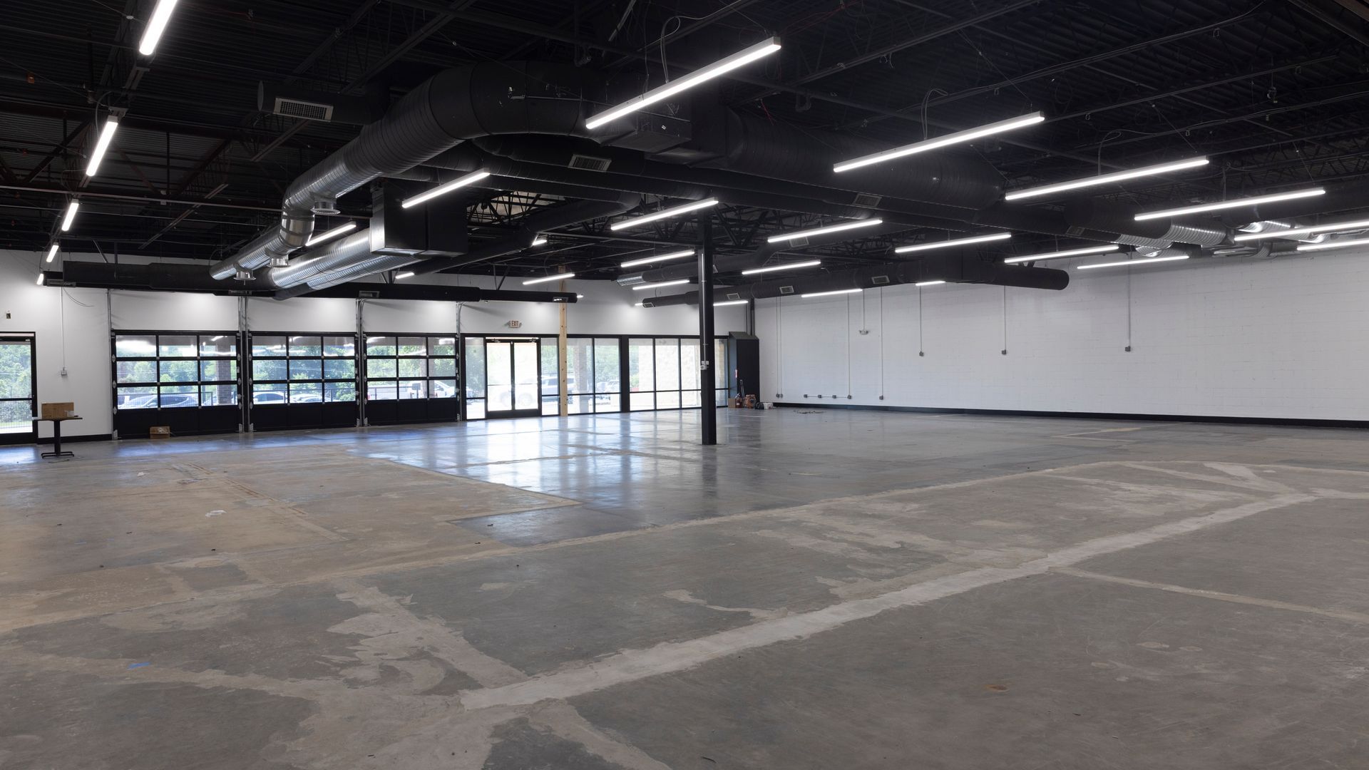 Empty industrial showroom with polished concrete floor, black ceiling lights, and large front windows.