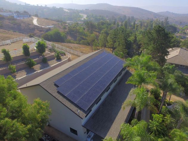 Rooftop solar panels on a white building amid trees and rolling hills on a sunny day