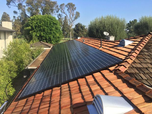 Solar panels installed on a terracotta-tiled roof beside trees and neighboring houses.