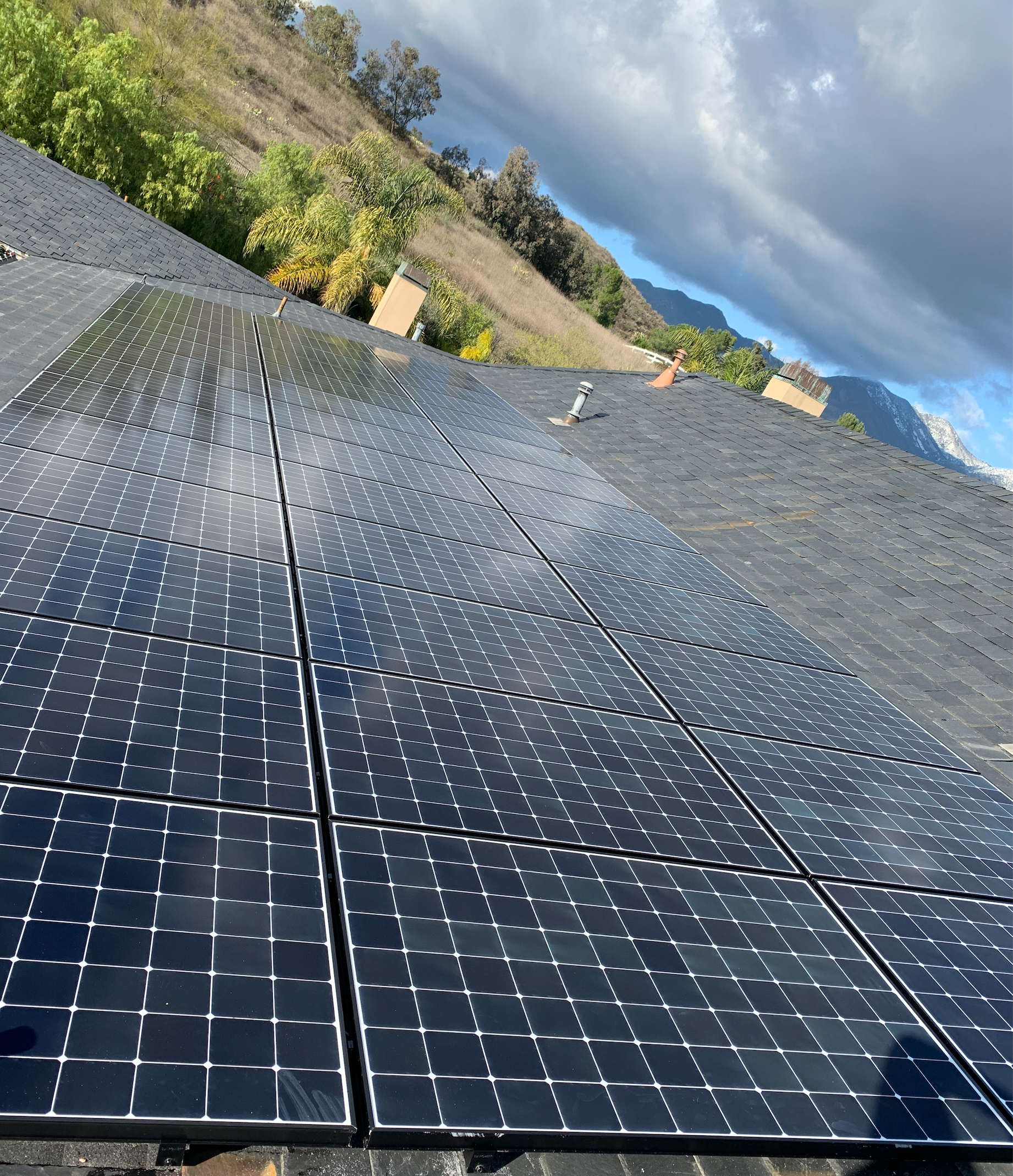 Rows of solar panels on a hillside under a cloudy sky, viewed at an angle.