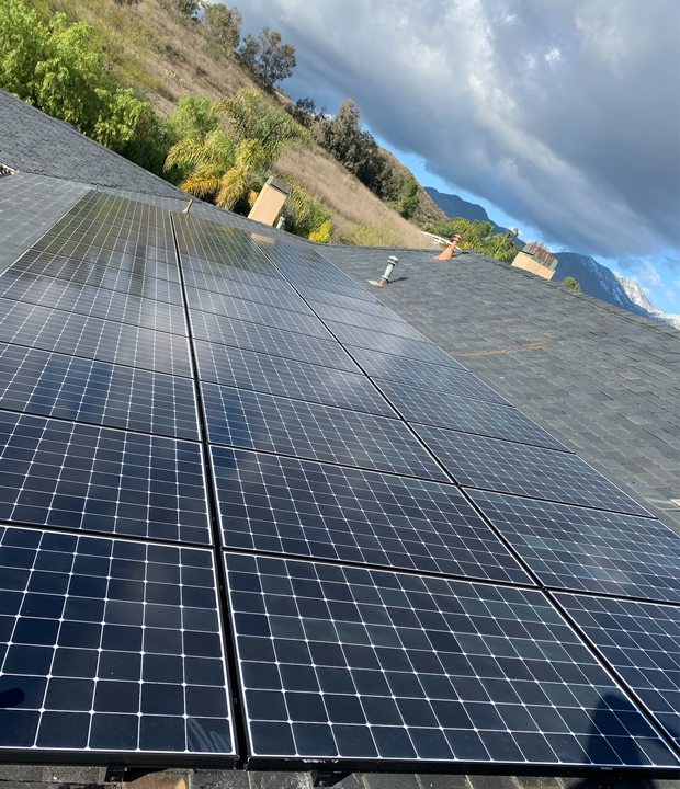 Rows of solar panels on a hillside under a cloudy sky, viewed at an angle.