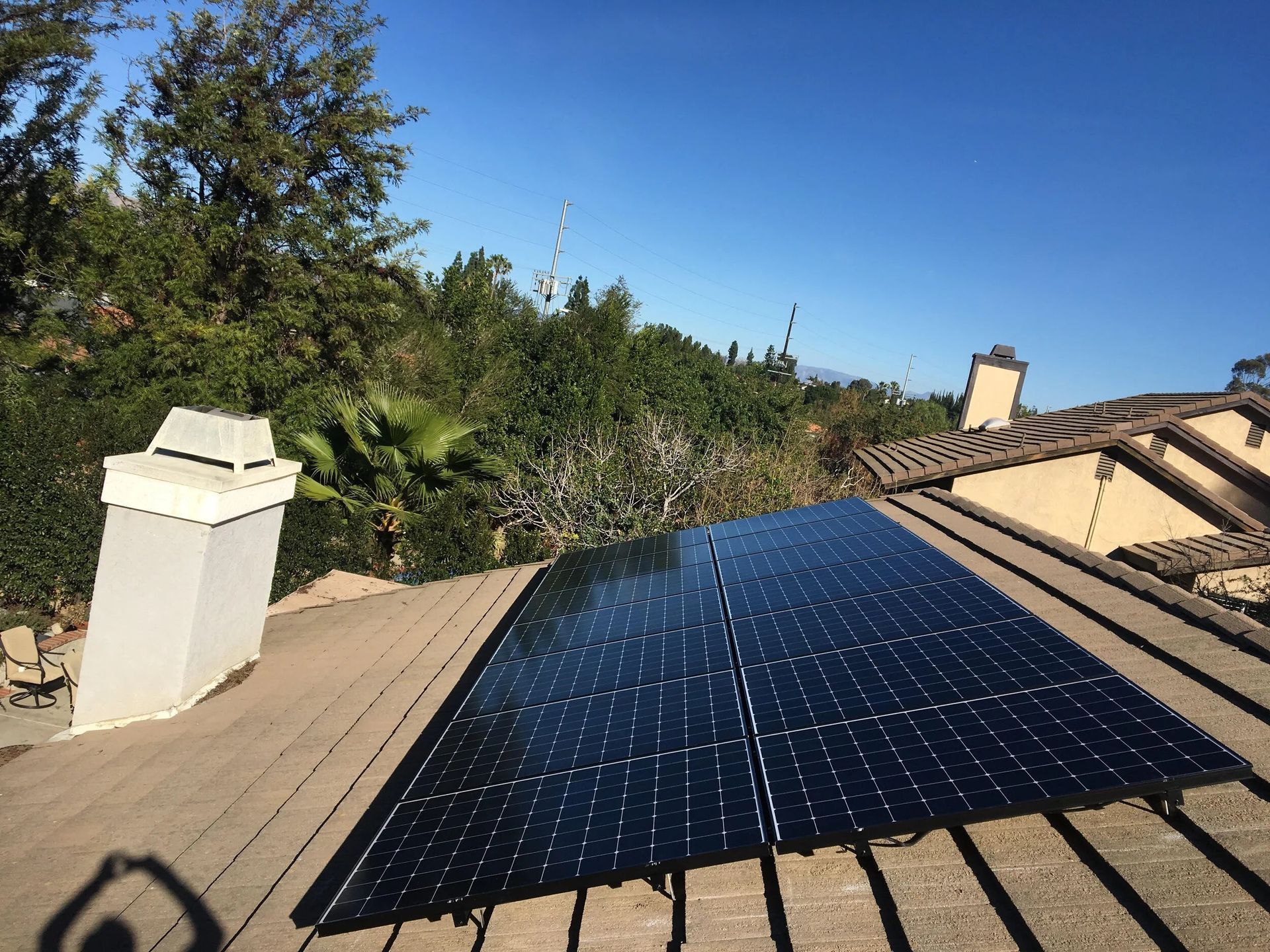Solar panels on a tan rooftop under a clear blue sky, with trees and a chimney nearby.