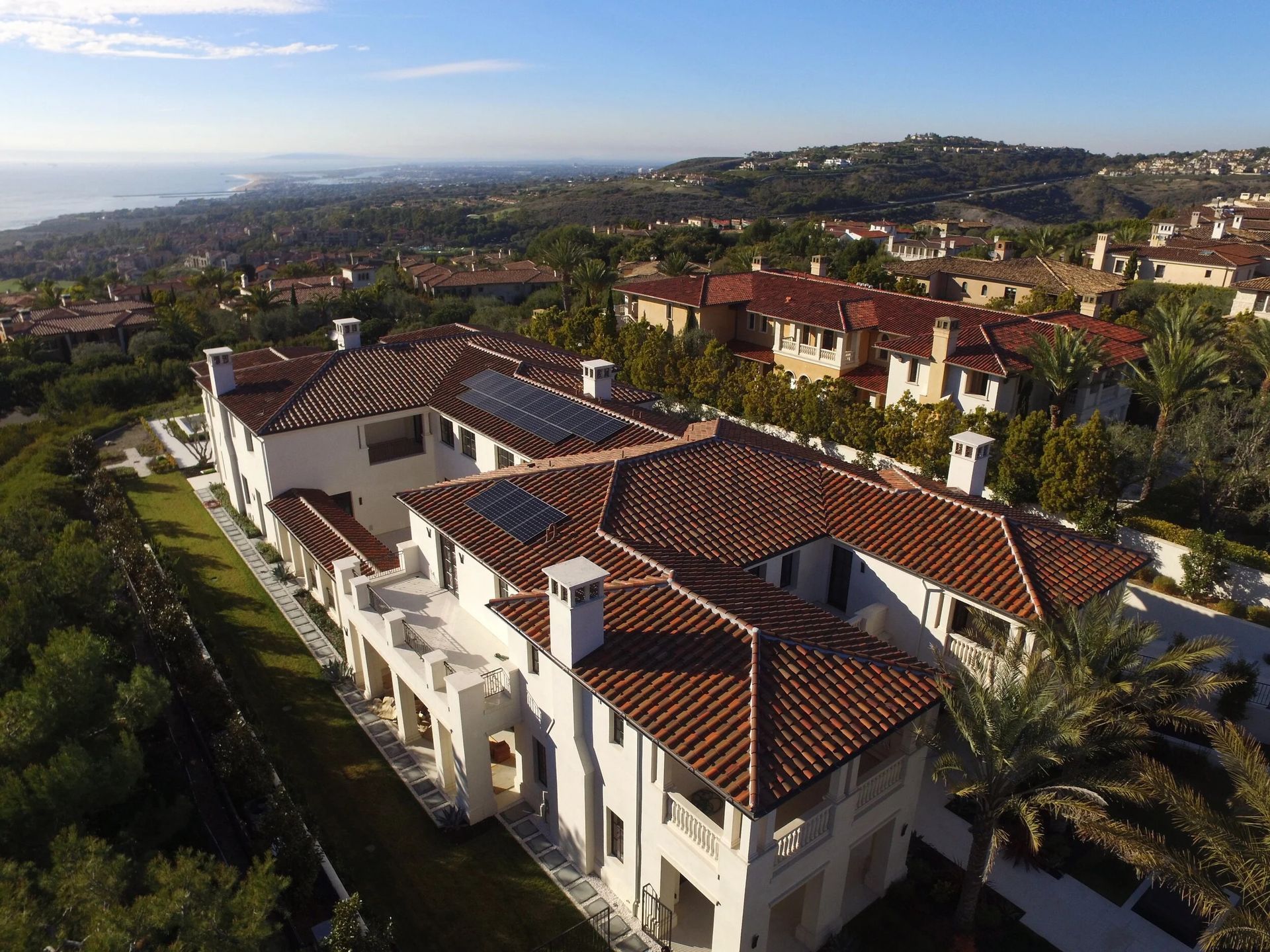 Aerial view of a white villa with red-tiled roofs in a hillside residential neighborhood
