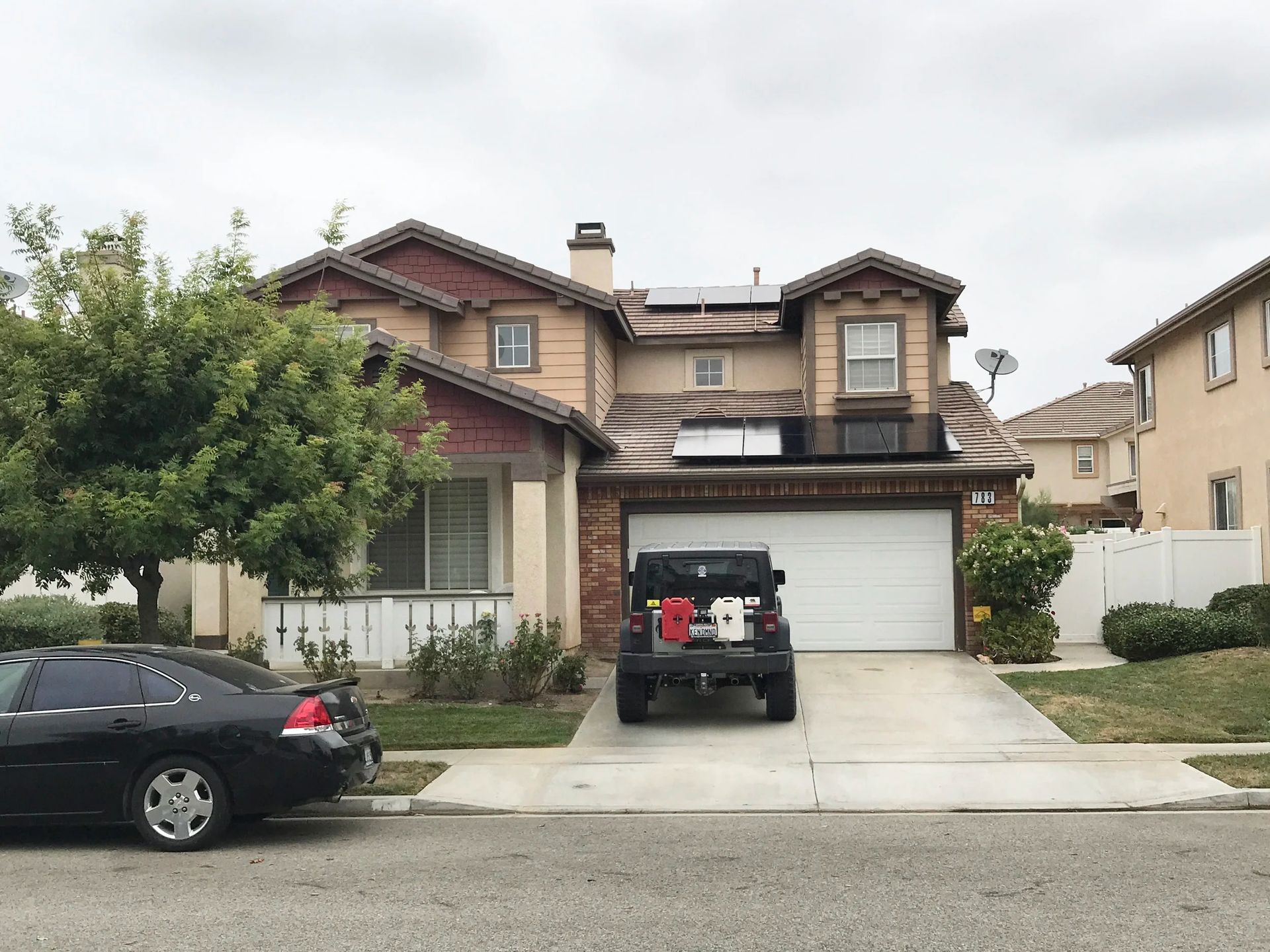 Two-story suburban house with a black SUV in the driveway and a black sedan parked at the curb