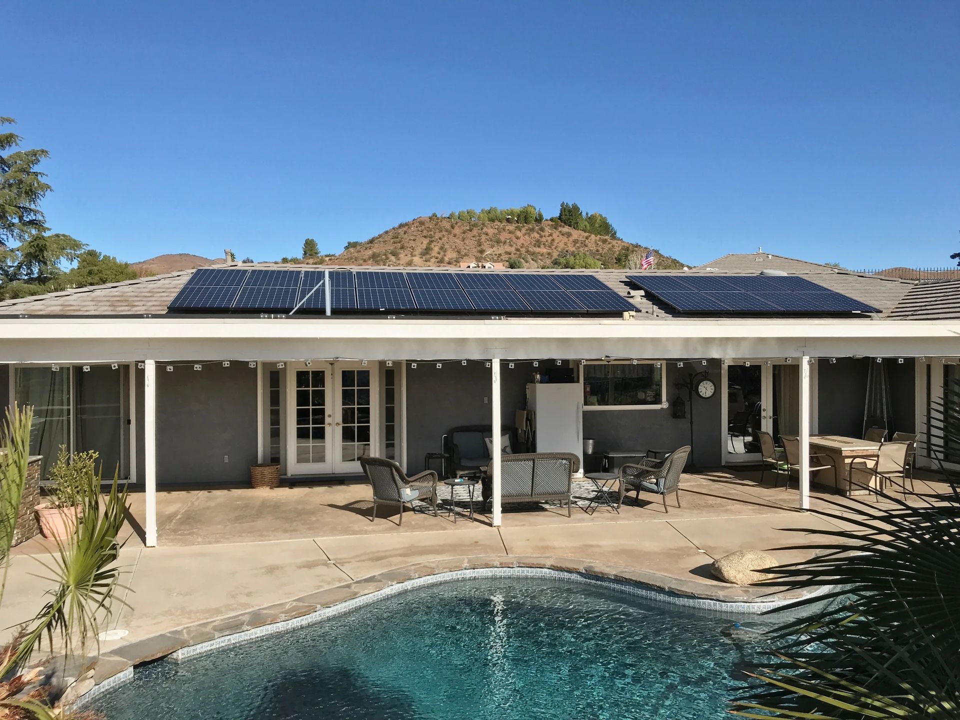 Backyard patio with pool, covered seating, and solar panels on the roof under a clear blue sky