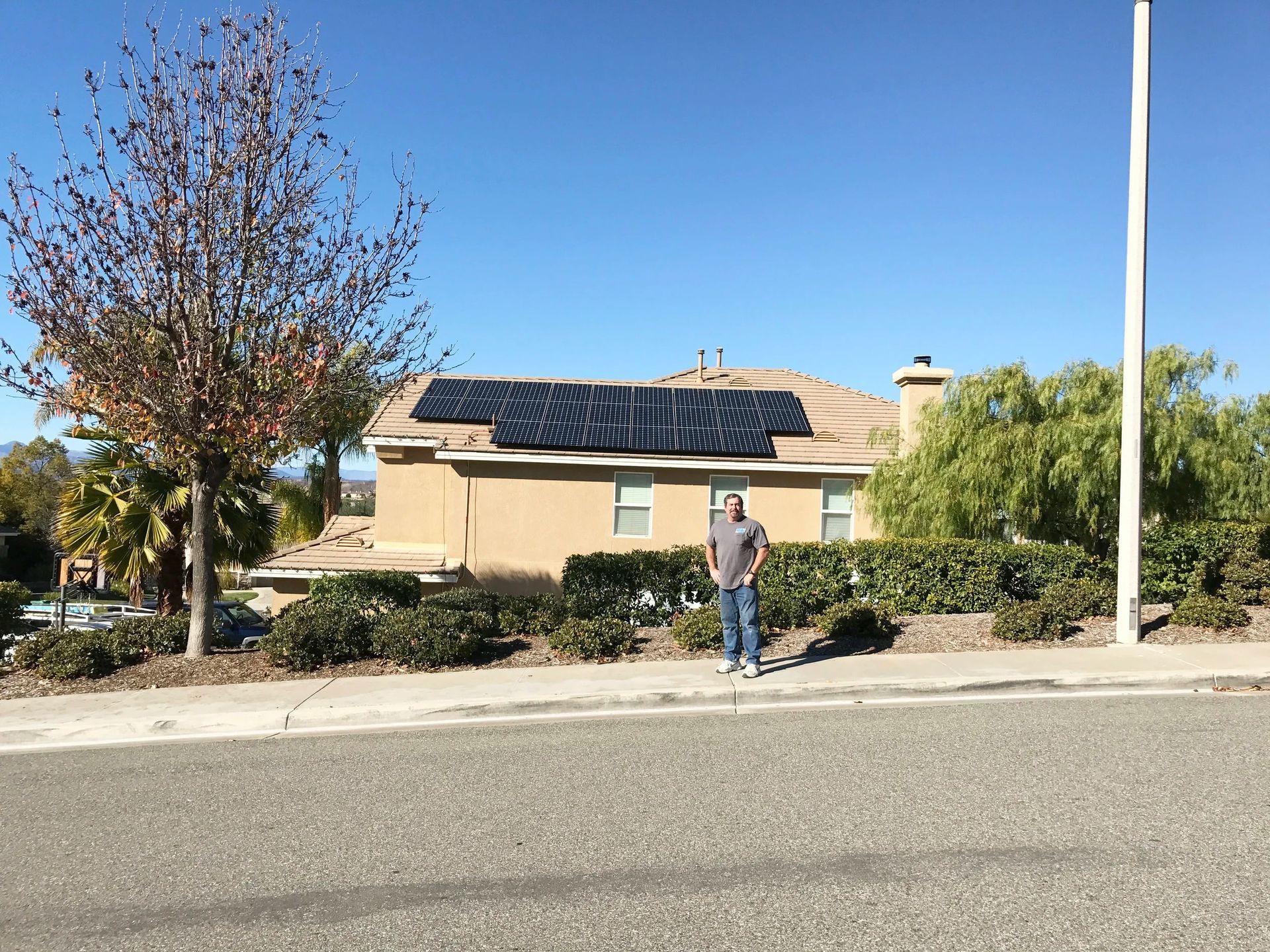 Residential street with a person standing near a beige house and solar panels under a clear blue sky