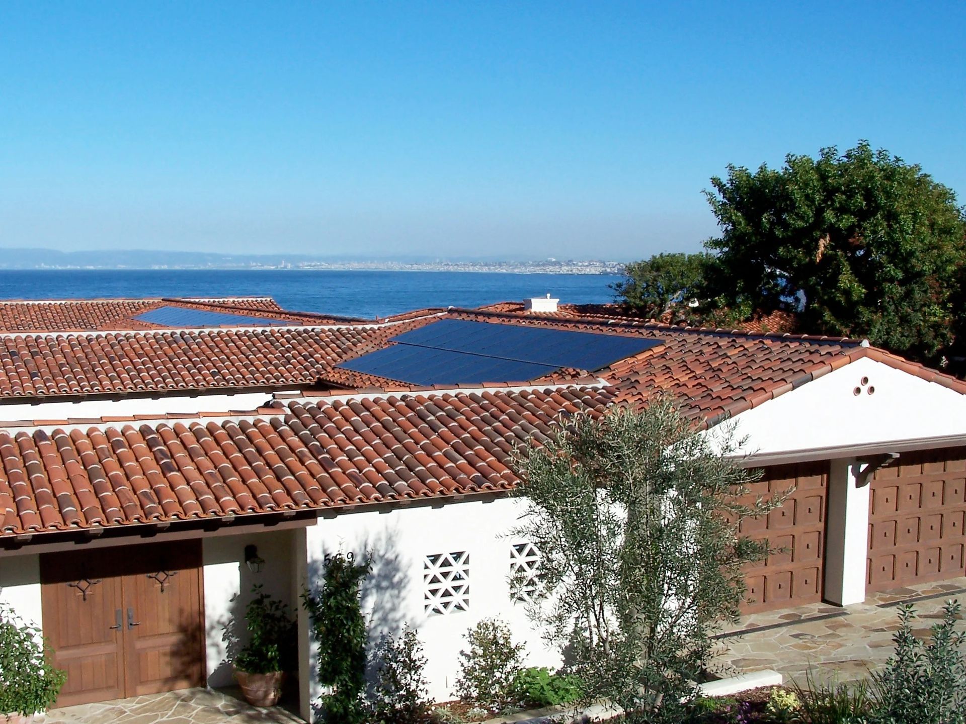 White houses with red-tiled roofs and solar panels overlooking the sea under a clear blue sky