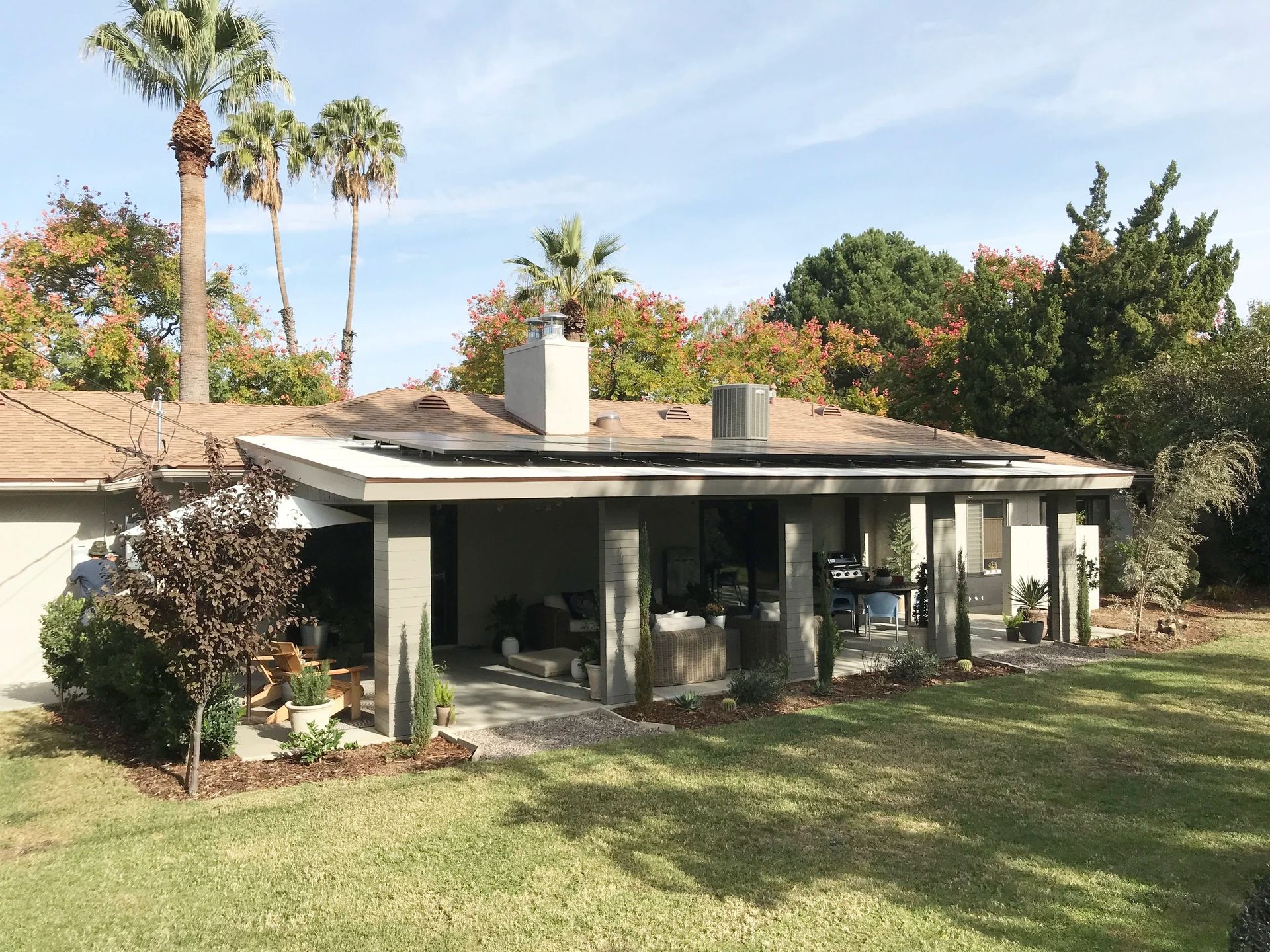 Single-story house with a covered patio, surrounded by a grassy yard and tall palm trees.