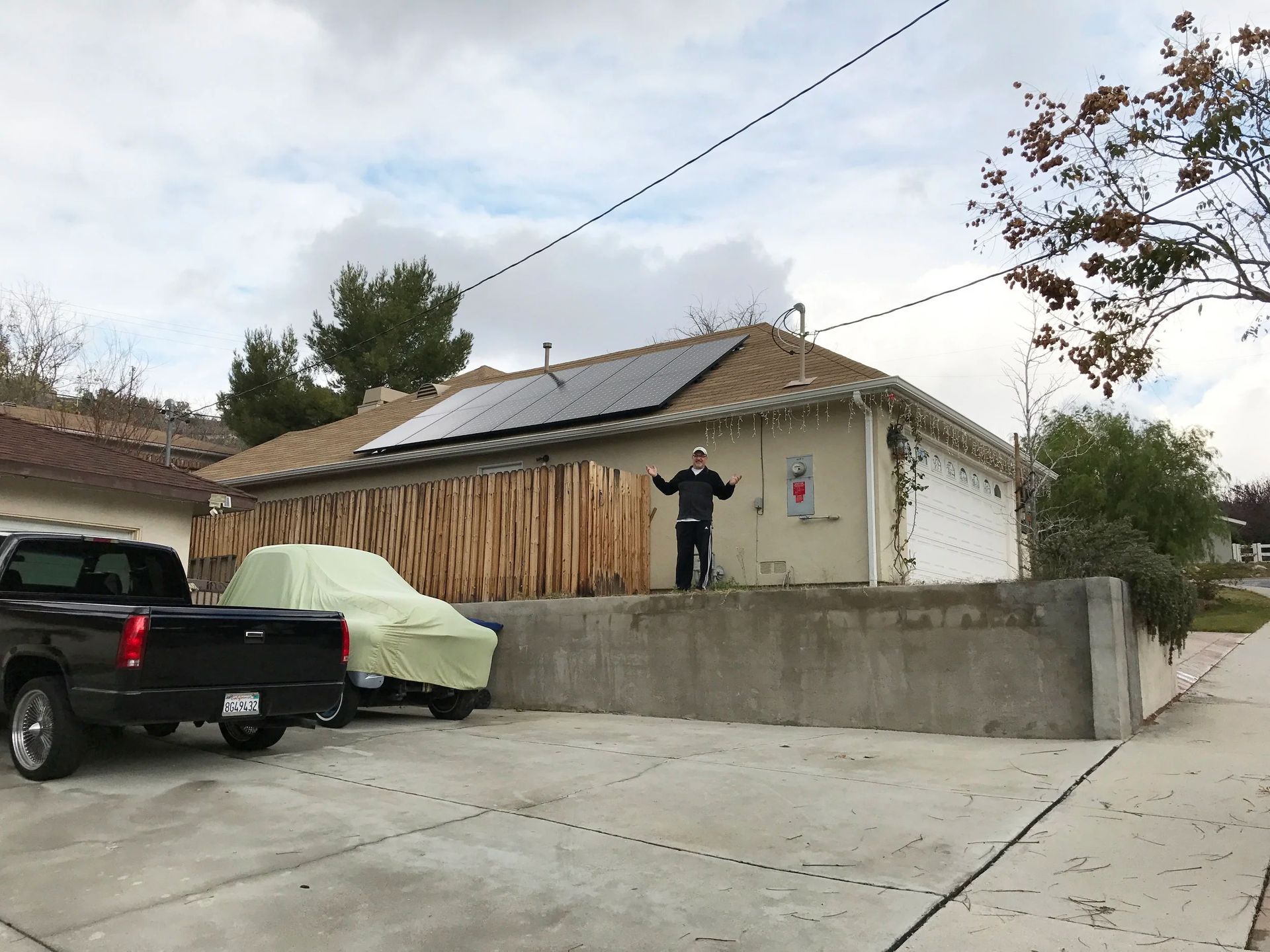 Person standing on a concrete driveway beside a pickup truck and house with solar panels