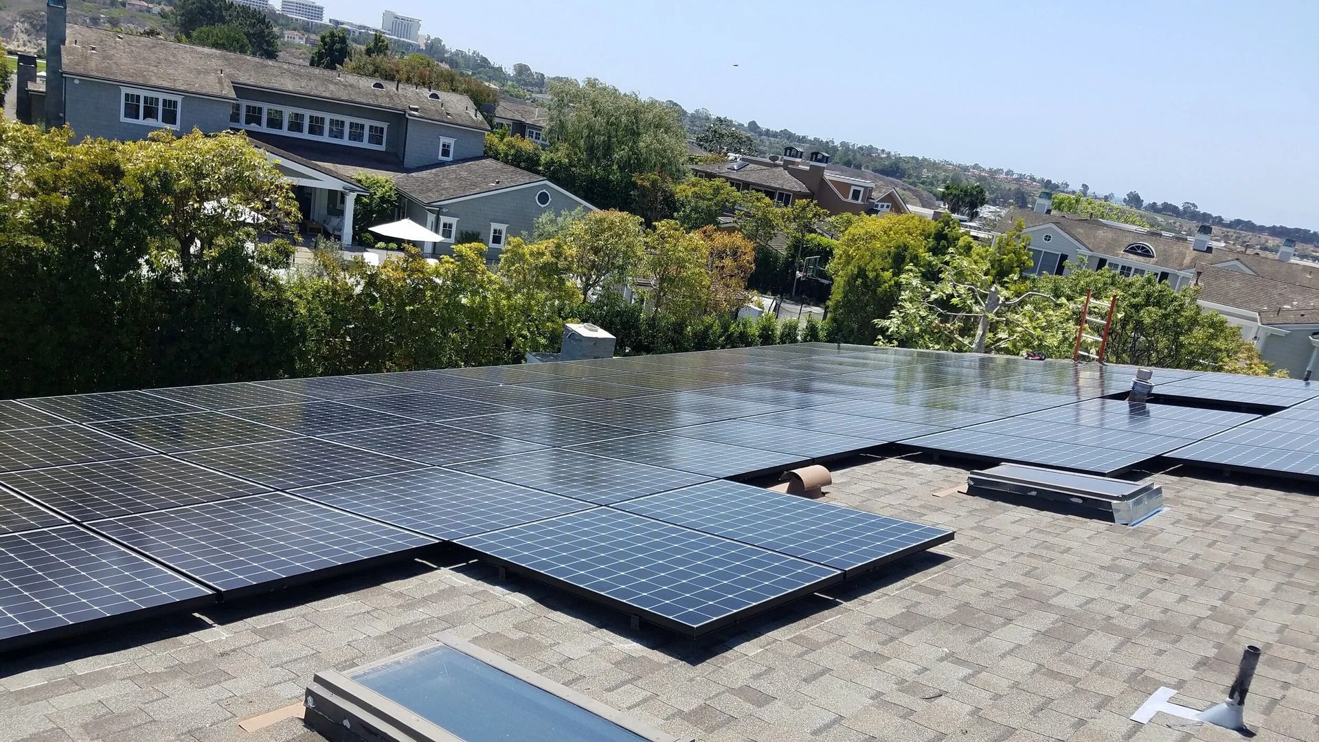 Solar panels covering a rooftop with suburban houses and trees in the background