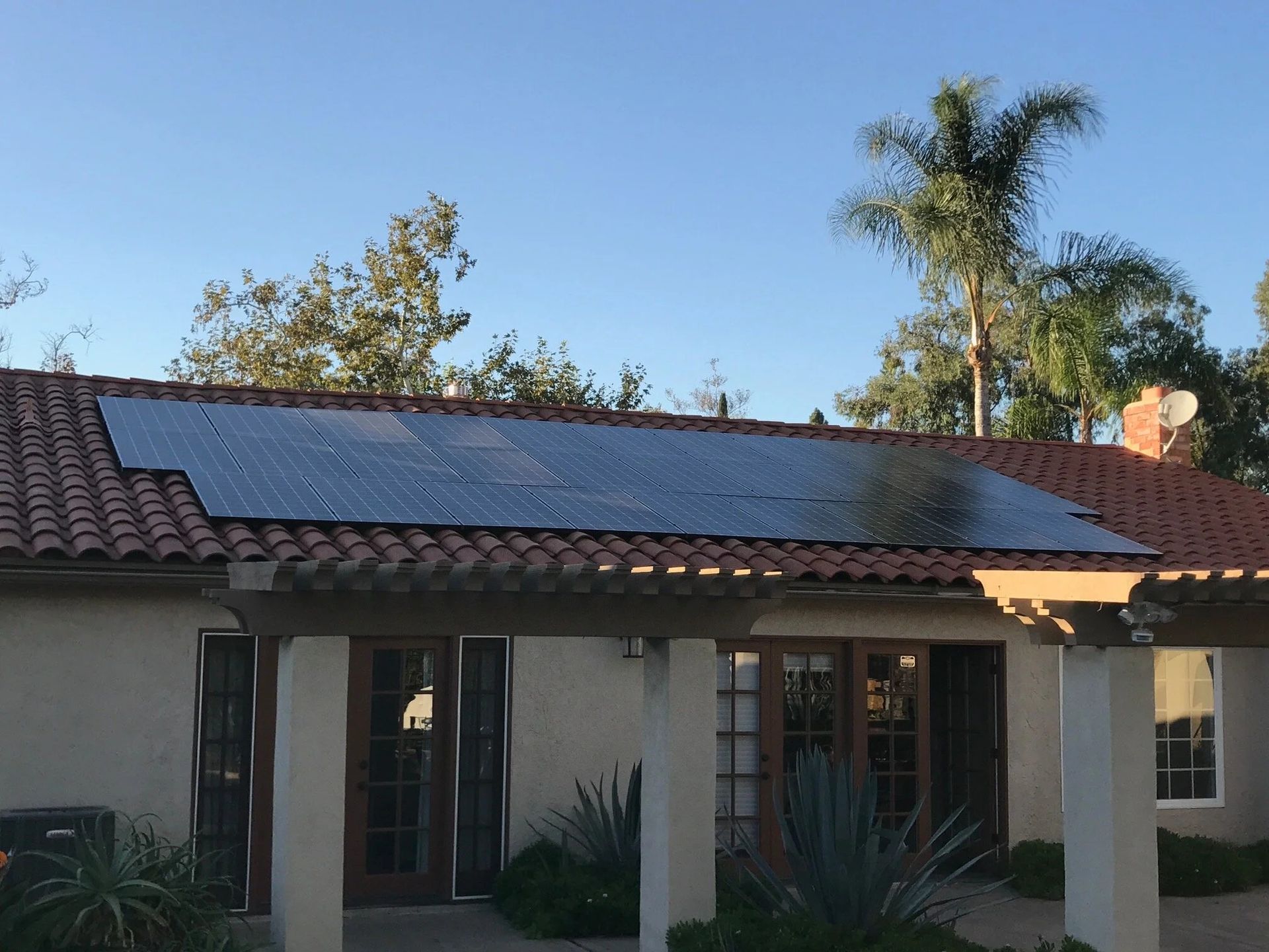 Single-story house with solar panels on the roof and palm trees in the yard.