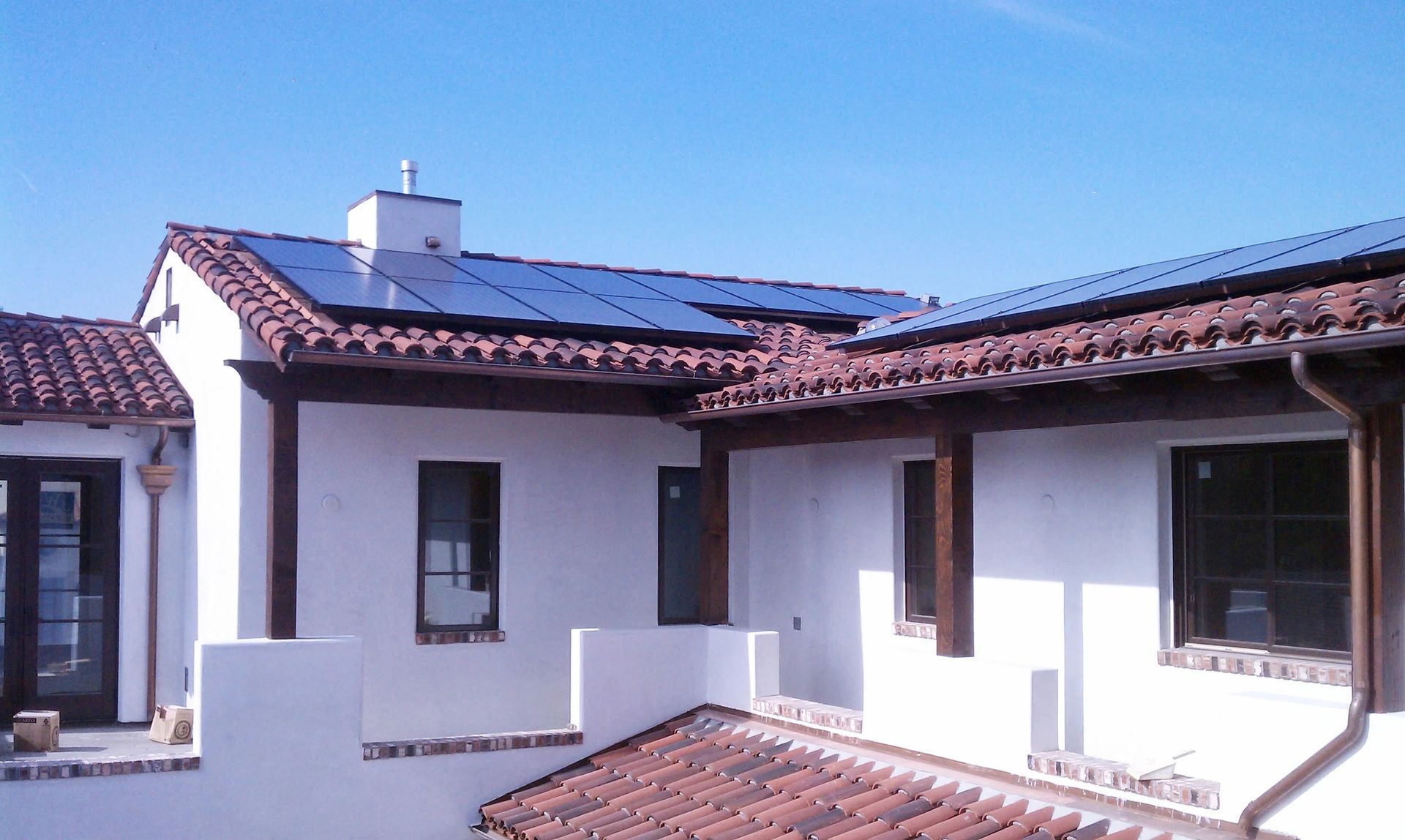 White stucco house with red-tile roof and solar panels under a clear blue sky