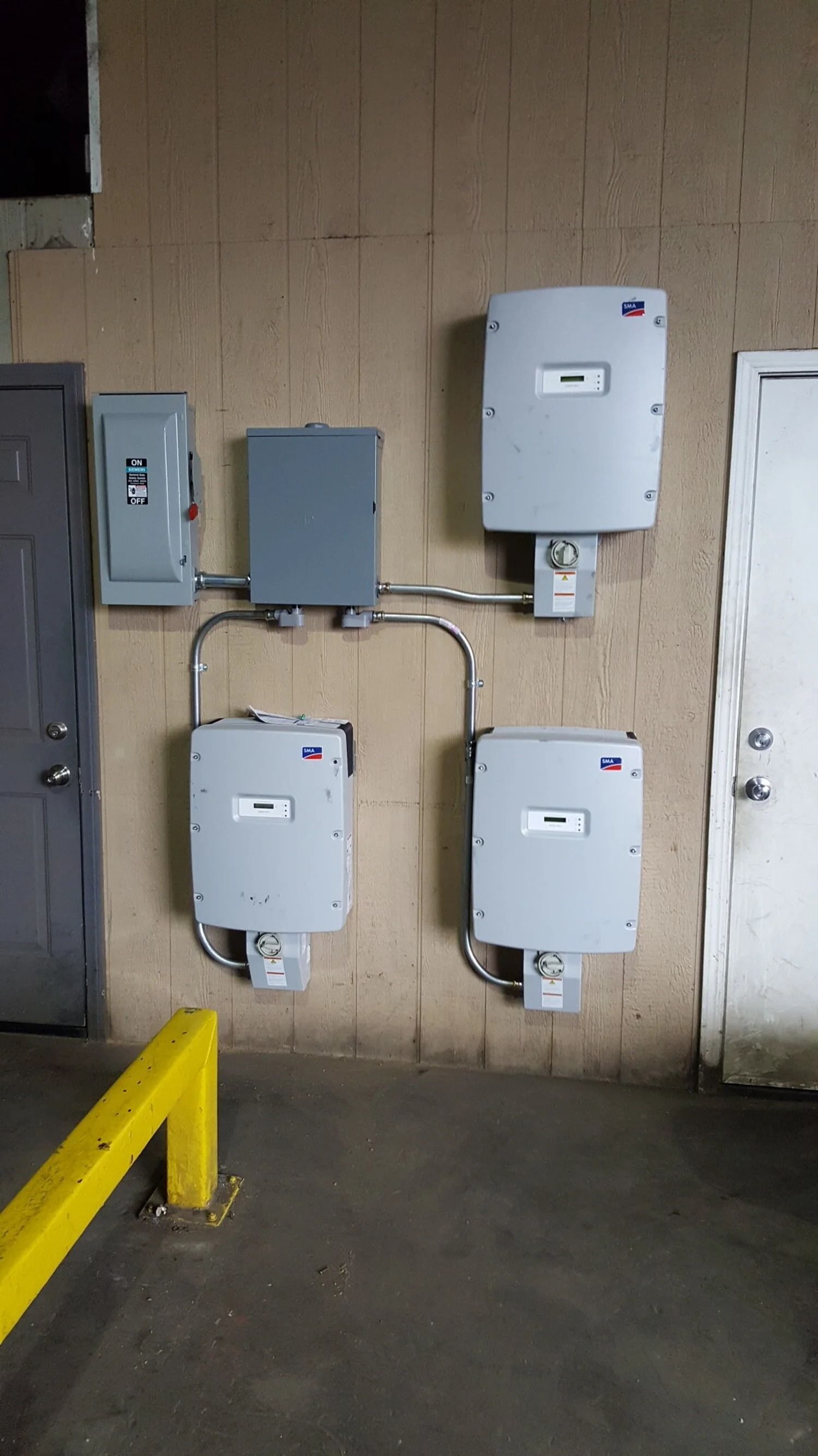 Several gray electrical meters and utility boxes mounted on a beige wall in a basement area.