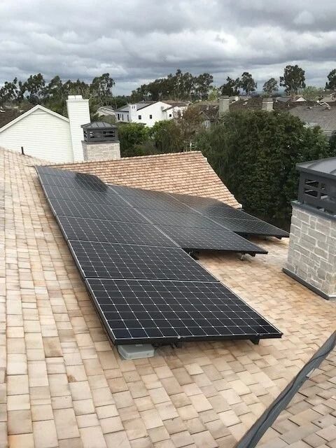 Solar panels installed on a shingled rooftop with neighboring houses and trees in the background.